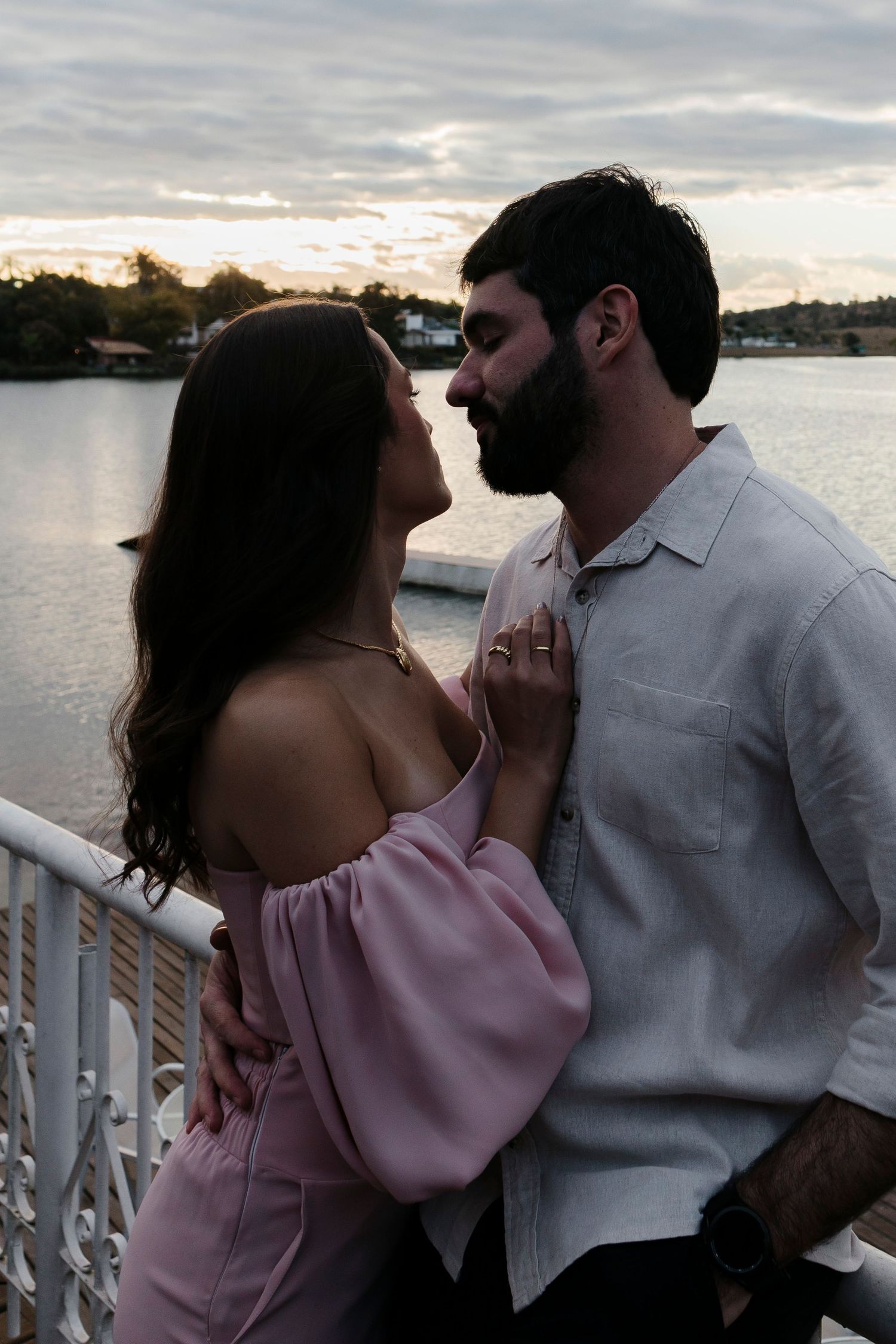 A couple embracing in a tender moment on a waterfront balcony at dusk.