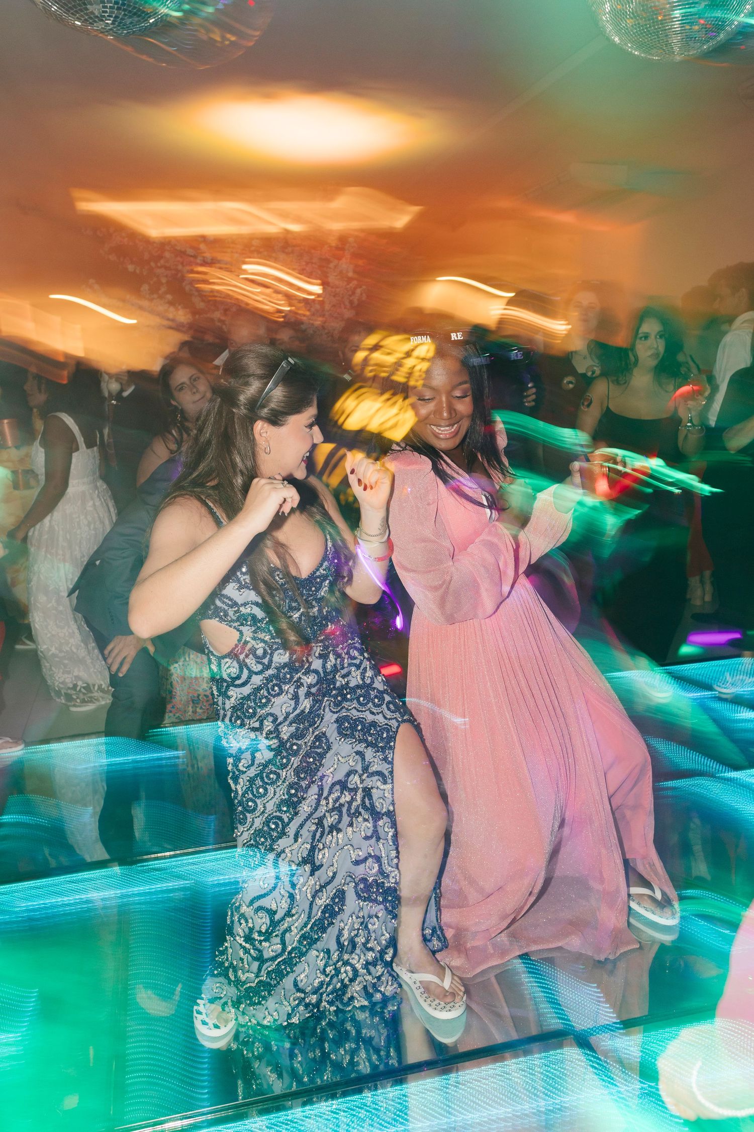 Party guests dancing under colorful lights in evening gowns at a lively celebration.