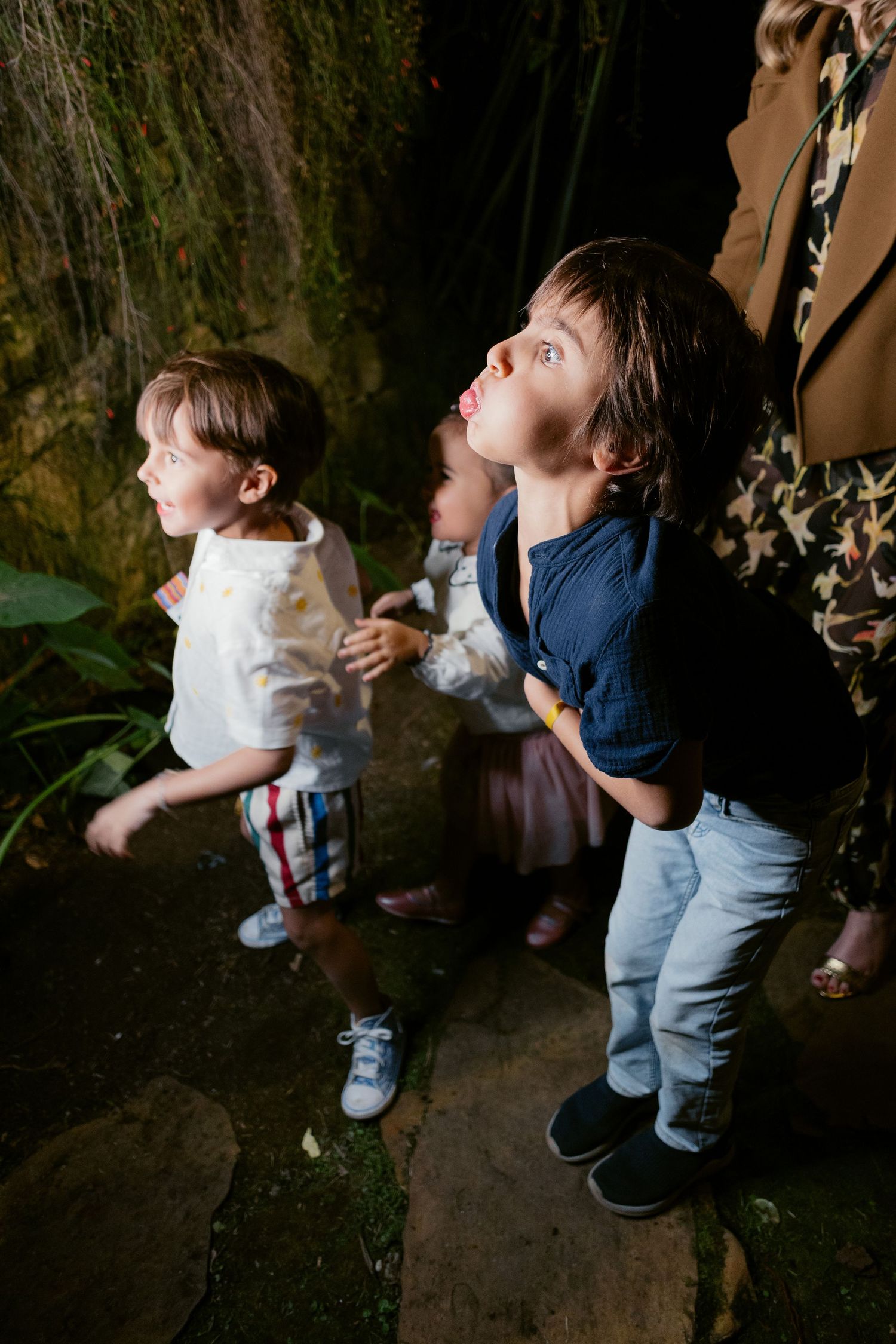 Young children look upward at something while standing in a dimly lit space.
