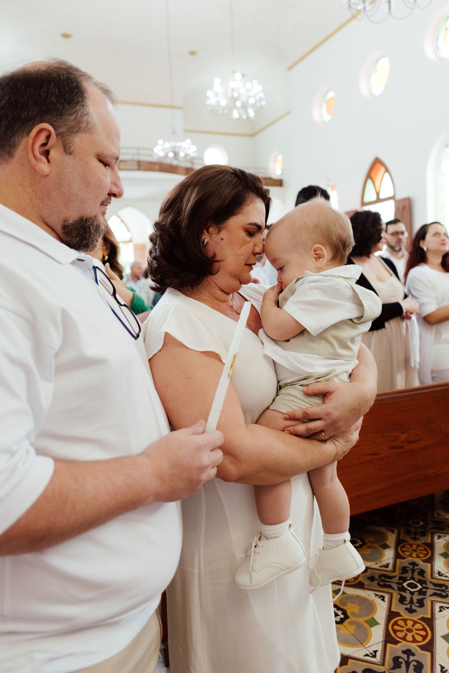 Parents in white clothing hold and comfort their babies during a church ceremony.