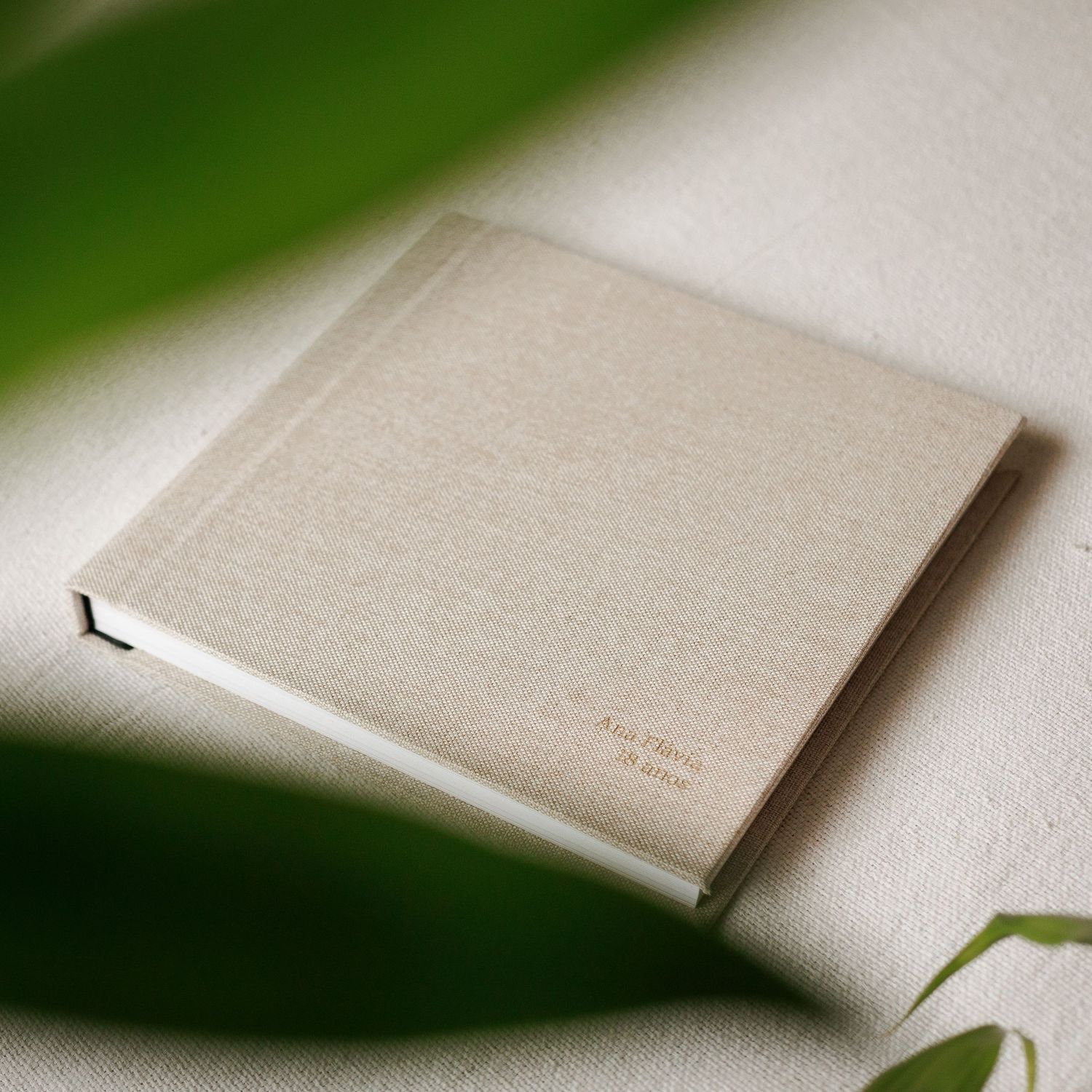 A minimalist beige linen book or photo album shown in various angles against a light background.
