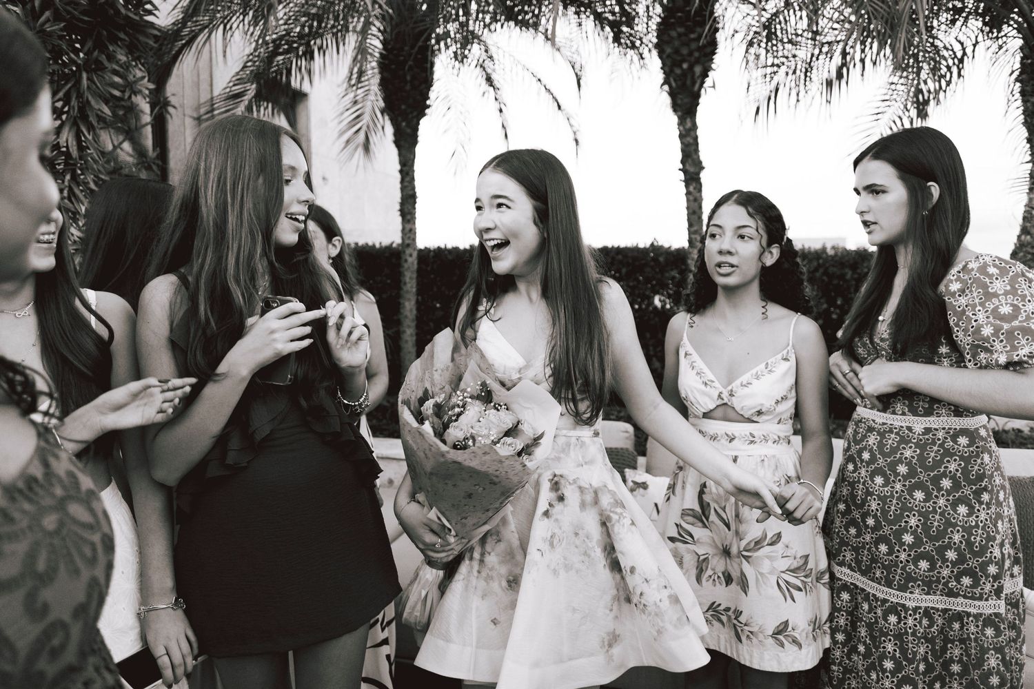 Black and white photo of a group enjoying conversation outdoors near palm trees.