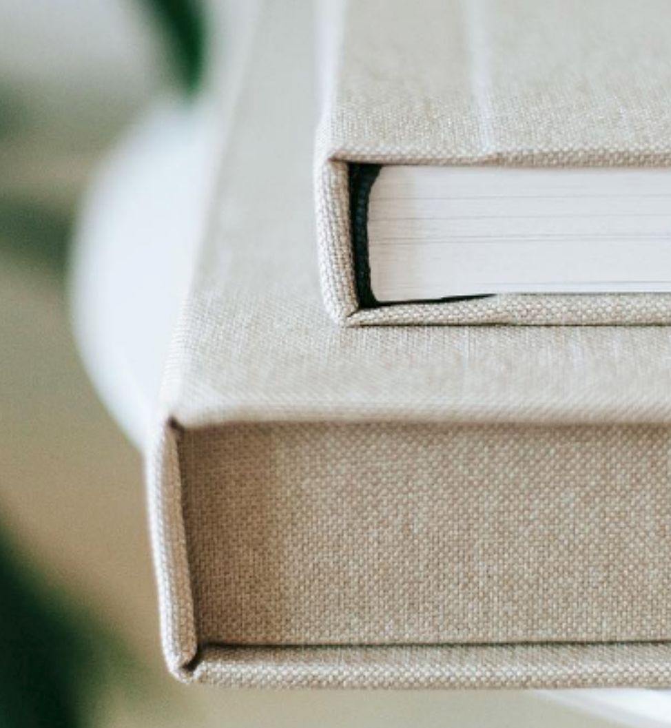Two hardcover books with linen texture covers stacked on a white surface, with soft natural lighting.