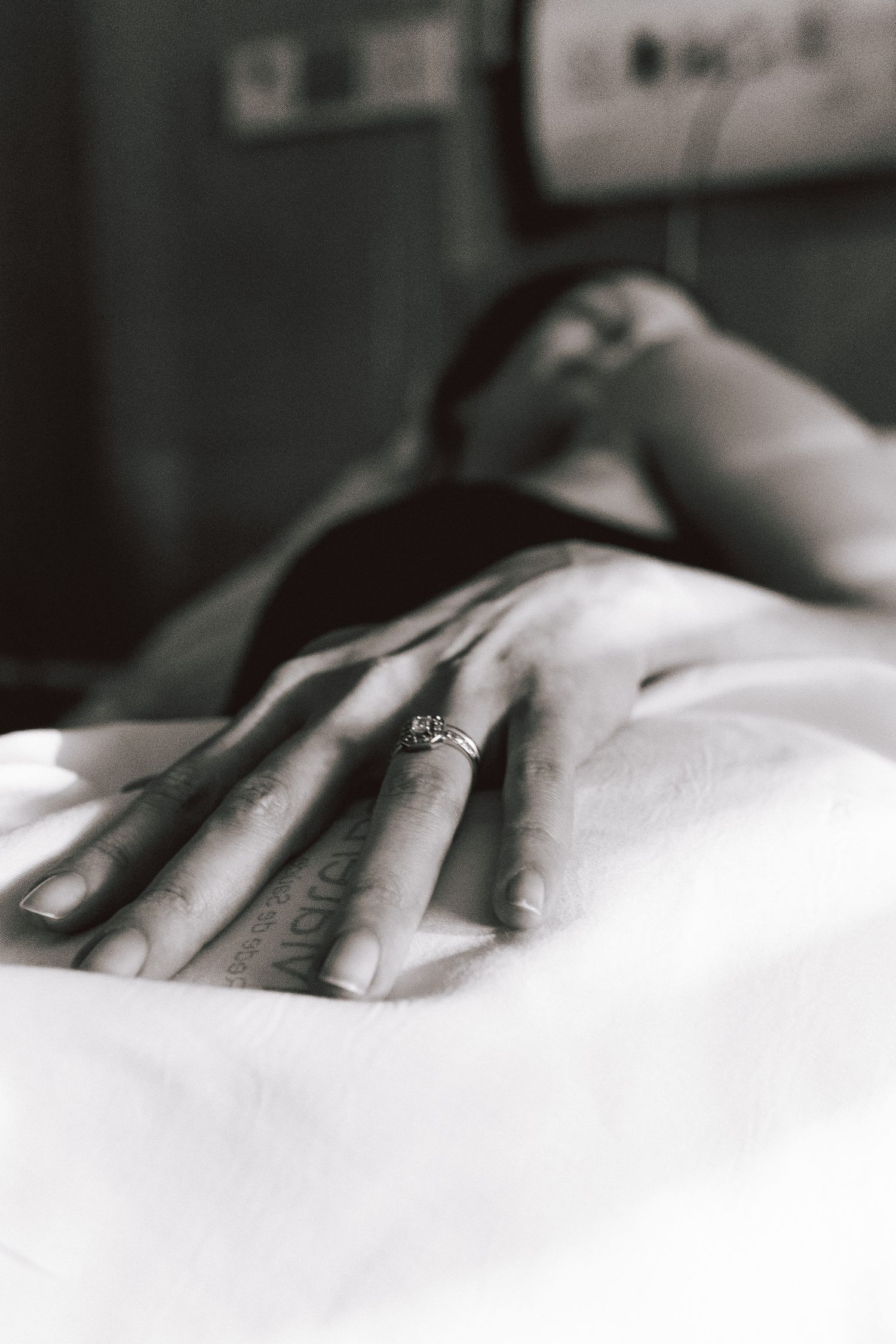 Black and white photo of a woman's hand with a diamond engagement ring resting on a white surface.