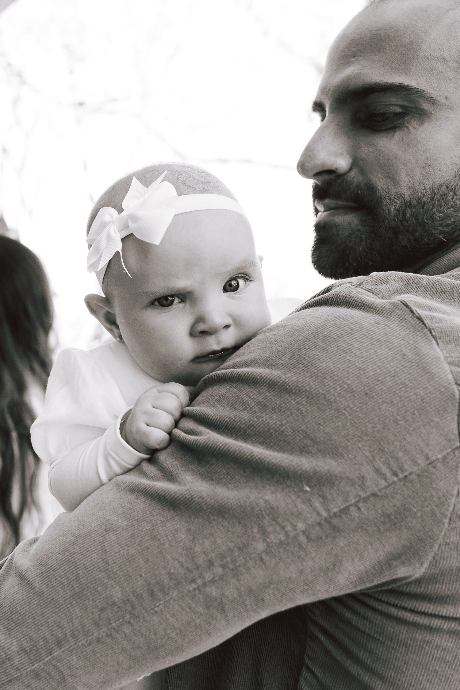 A tender moment captured in black and white showing a parent holding a baby wearing a white bow headband.