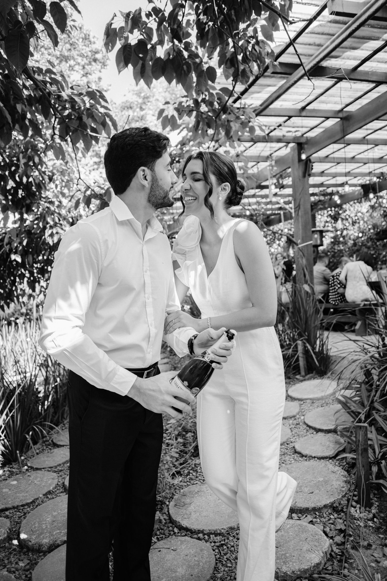 Black and white photo of a couple sharing an intimate moment under a garden trellis surrounded by greenery.
