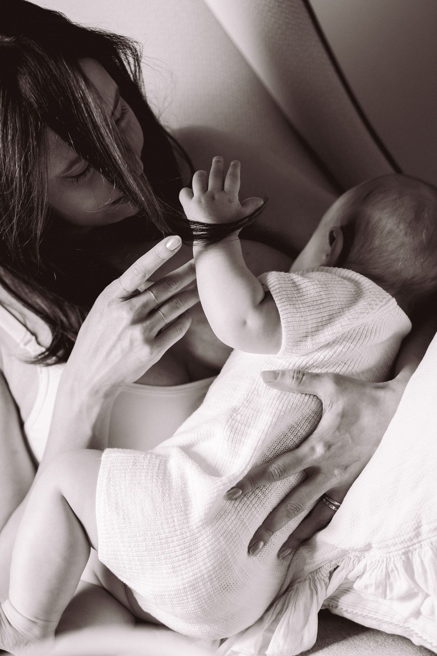 Black and white photo of a mother tenderly holding her newborn baby, the infant reaching up toward her face.