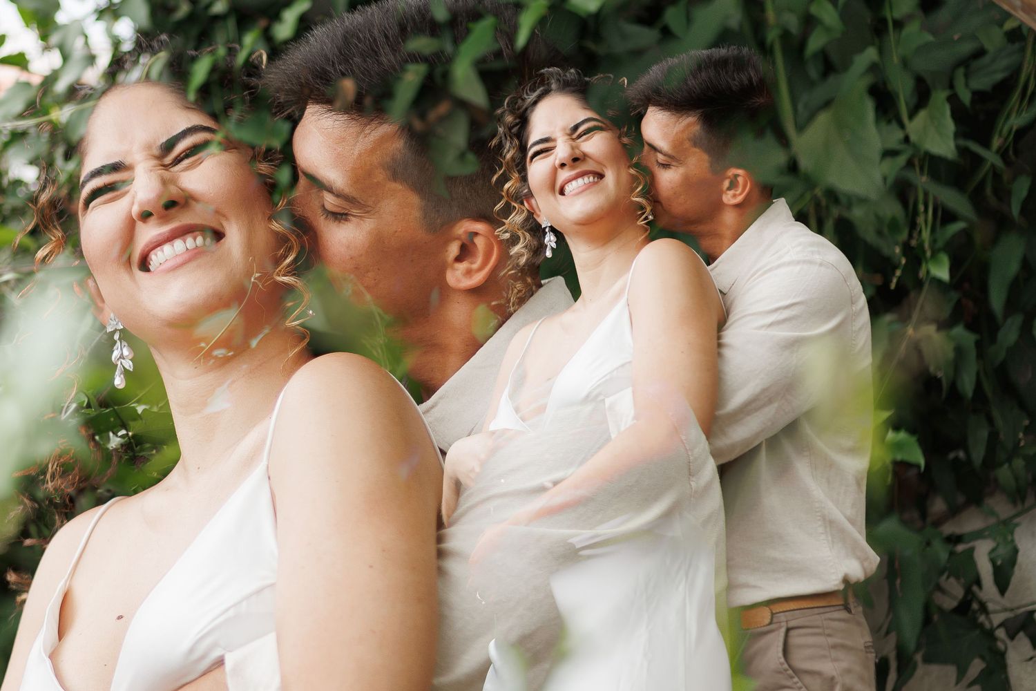 A romantic couple shares tender moments in a lush garden setting wearing white attire.