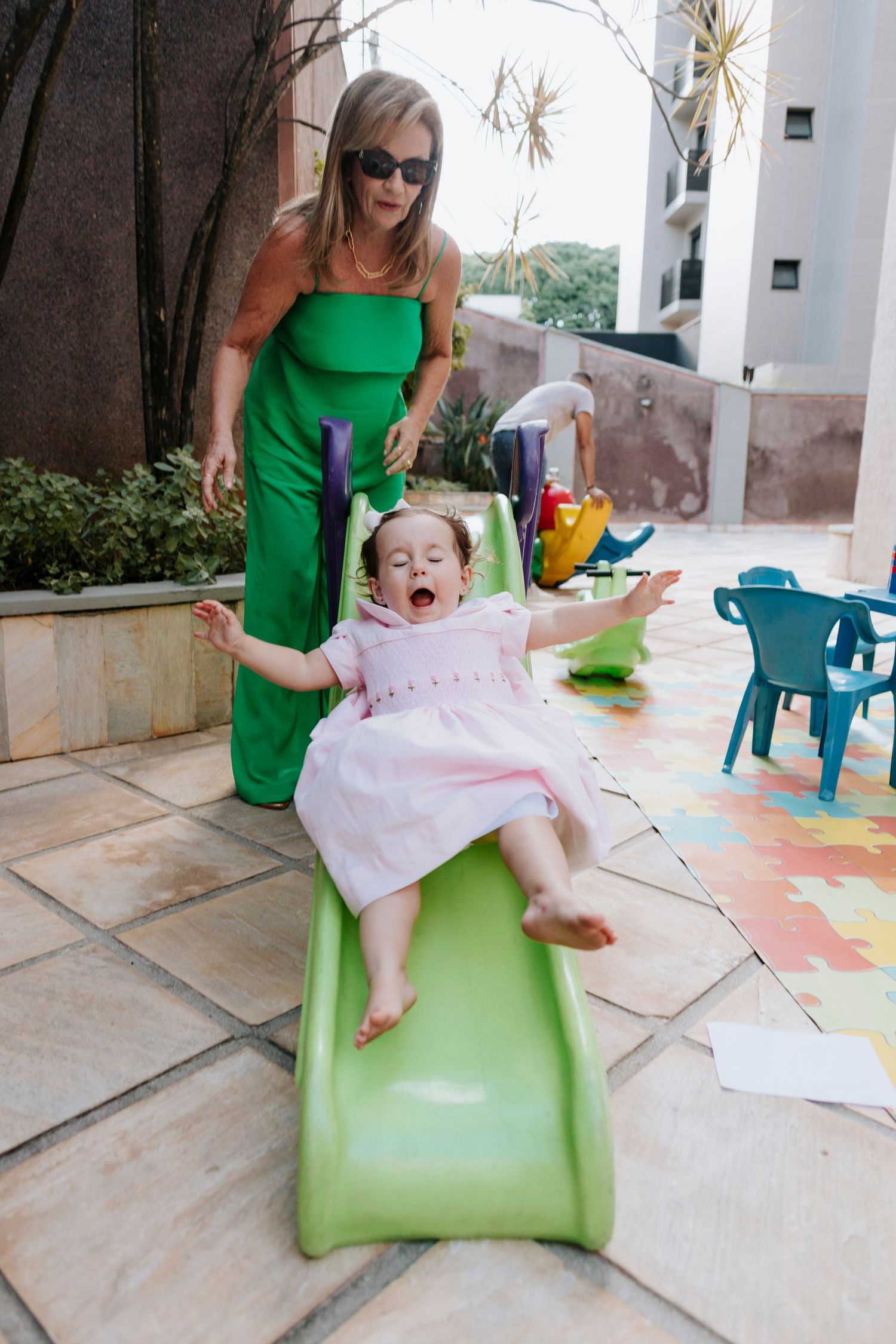 A child in a pink dress joyfully slides down a green playground slide.
