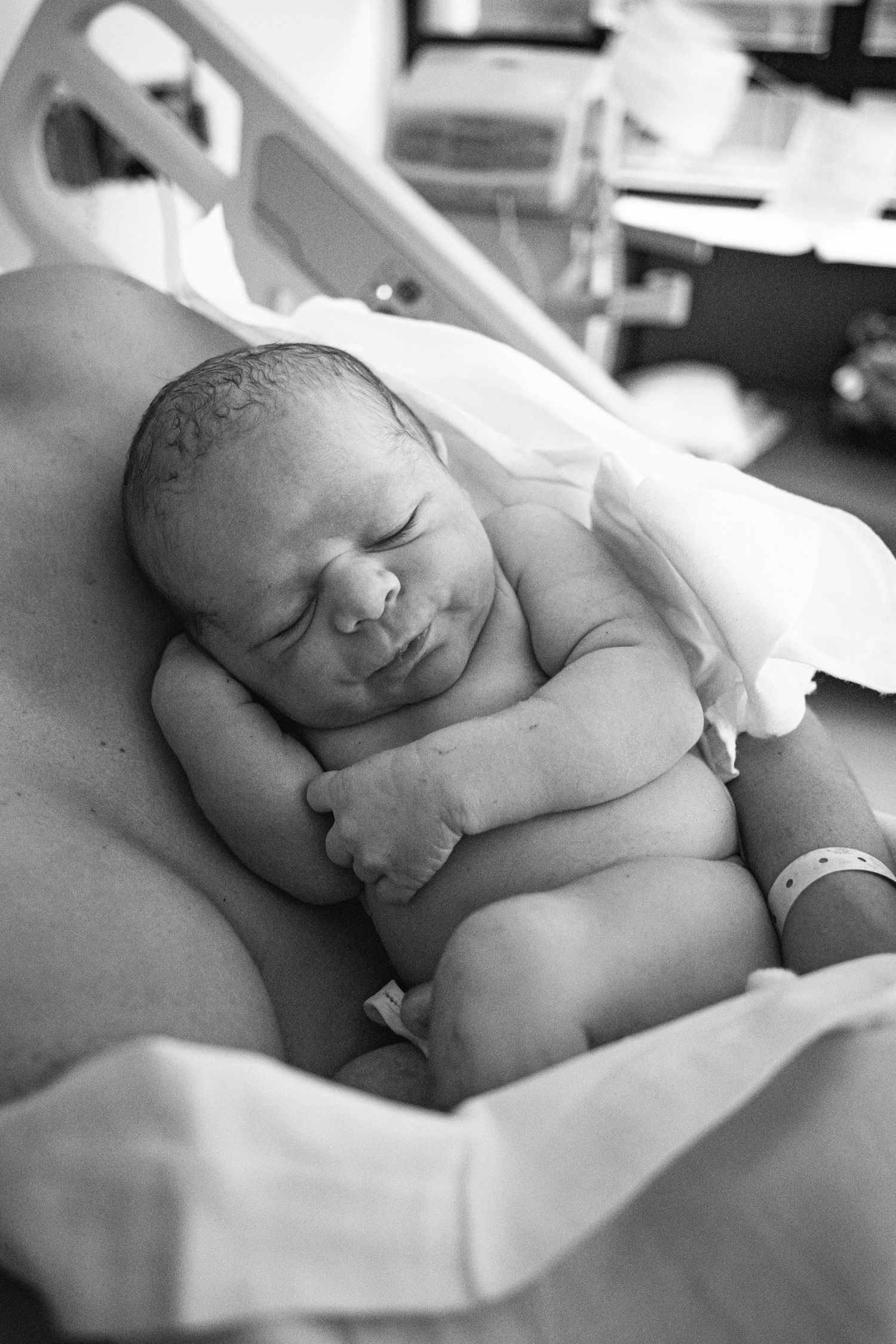 A peaceful newborn baby sleeping on their back in black and white.