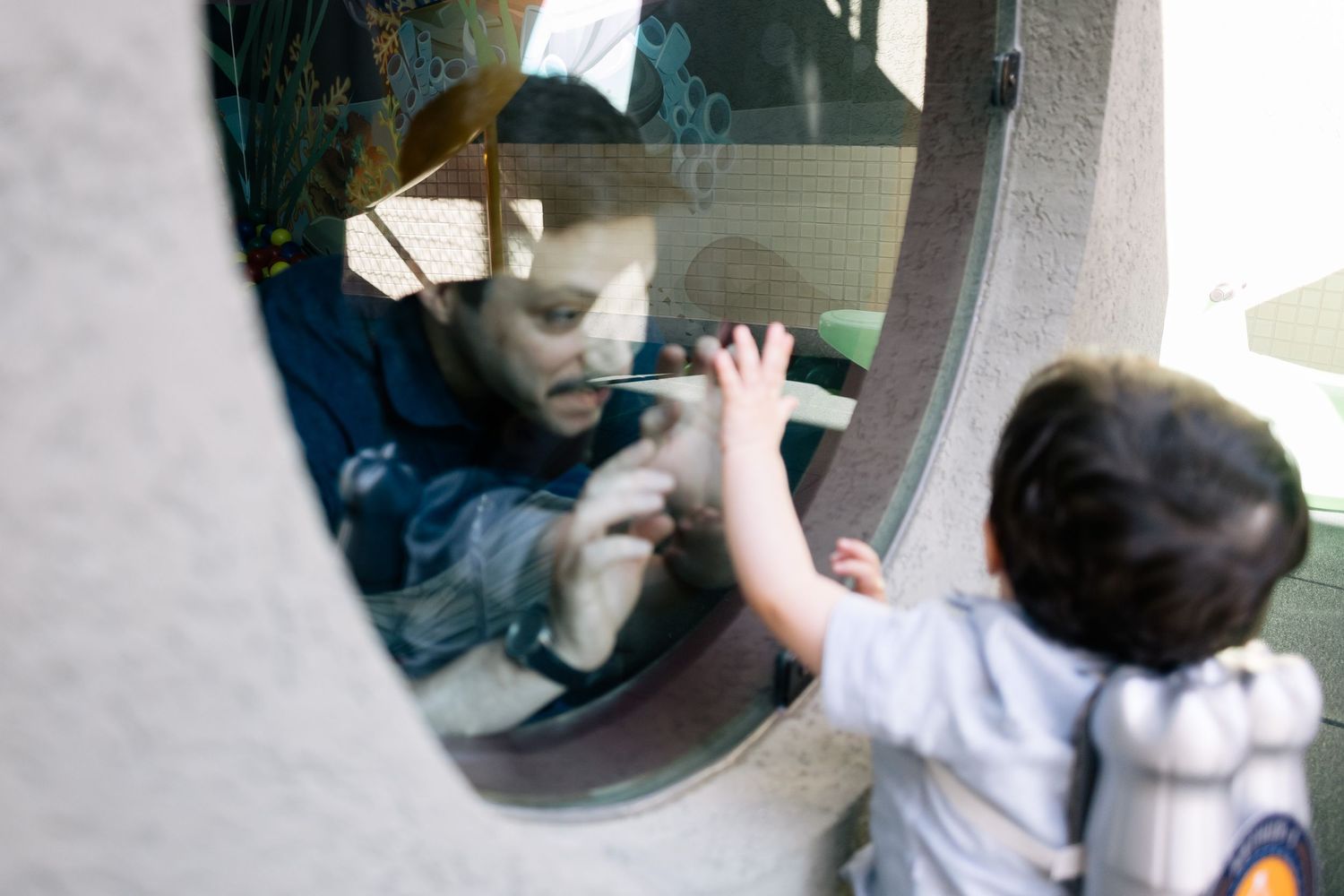 Man and toddler touching hands through a round window, sharing a tender moment of connection.