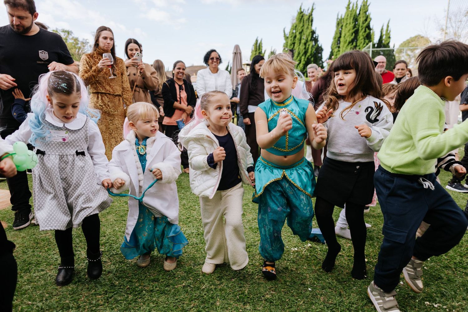 Wedding guests running and playing together on a grassy lawn during an outdoor celebration.