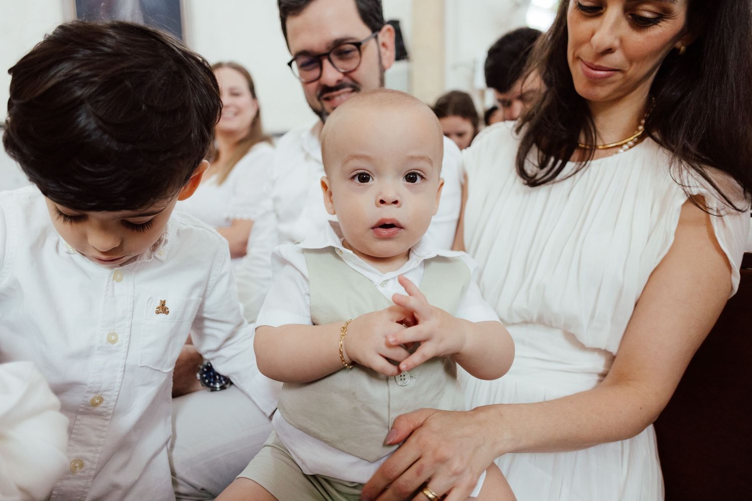 A series of family photos showing tender moments with a baby in white outfits against a light background.
