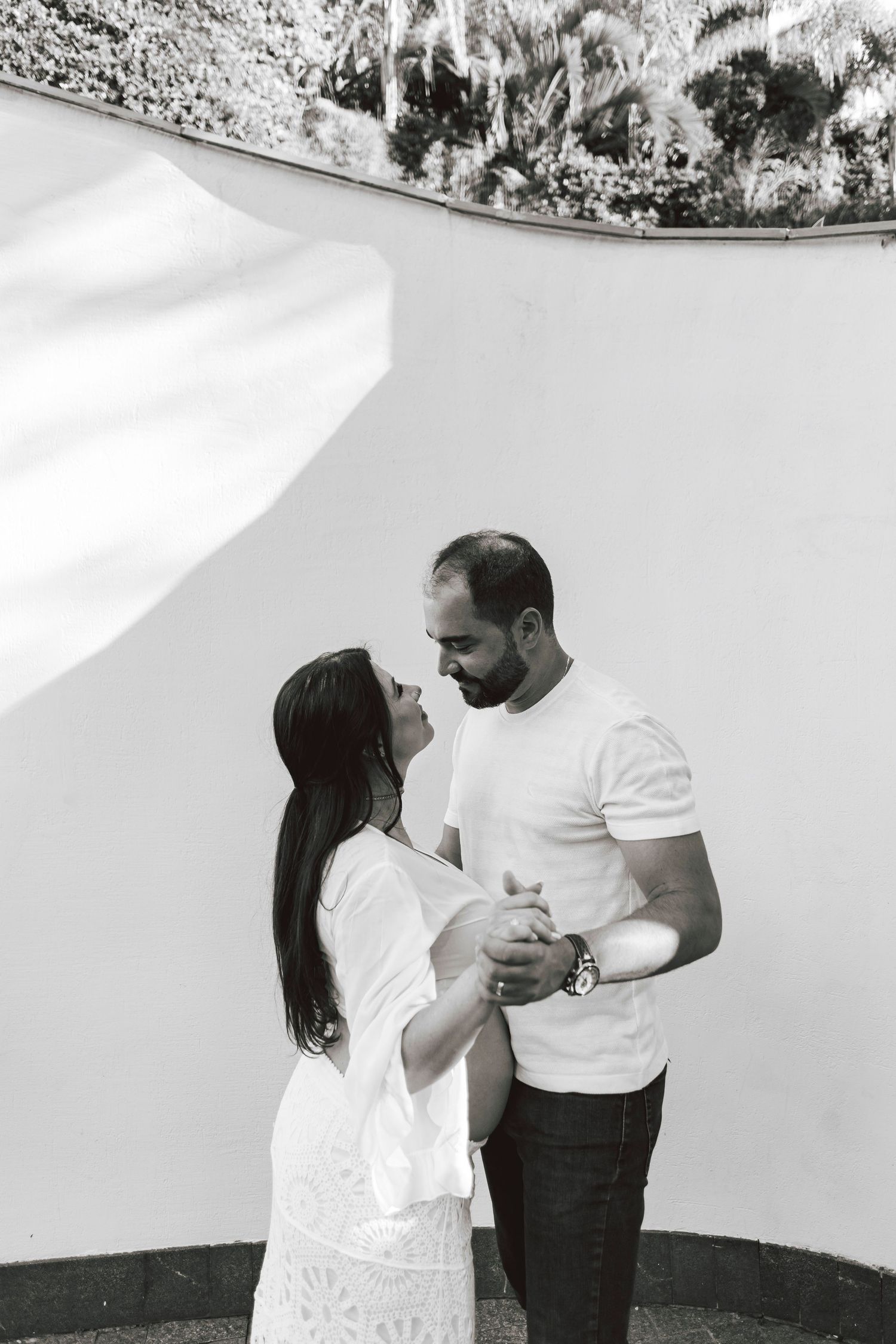 A couple in white clothing share an intimate moment against a light colored wall.