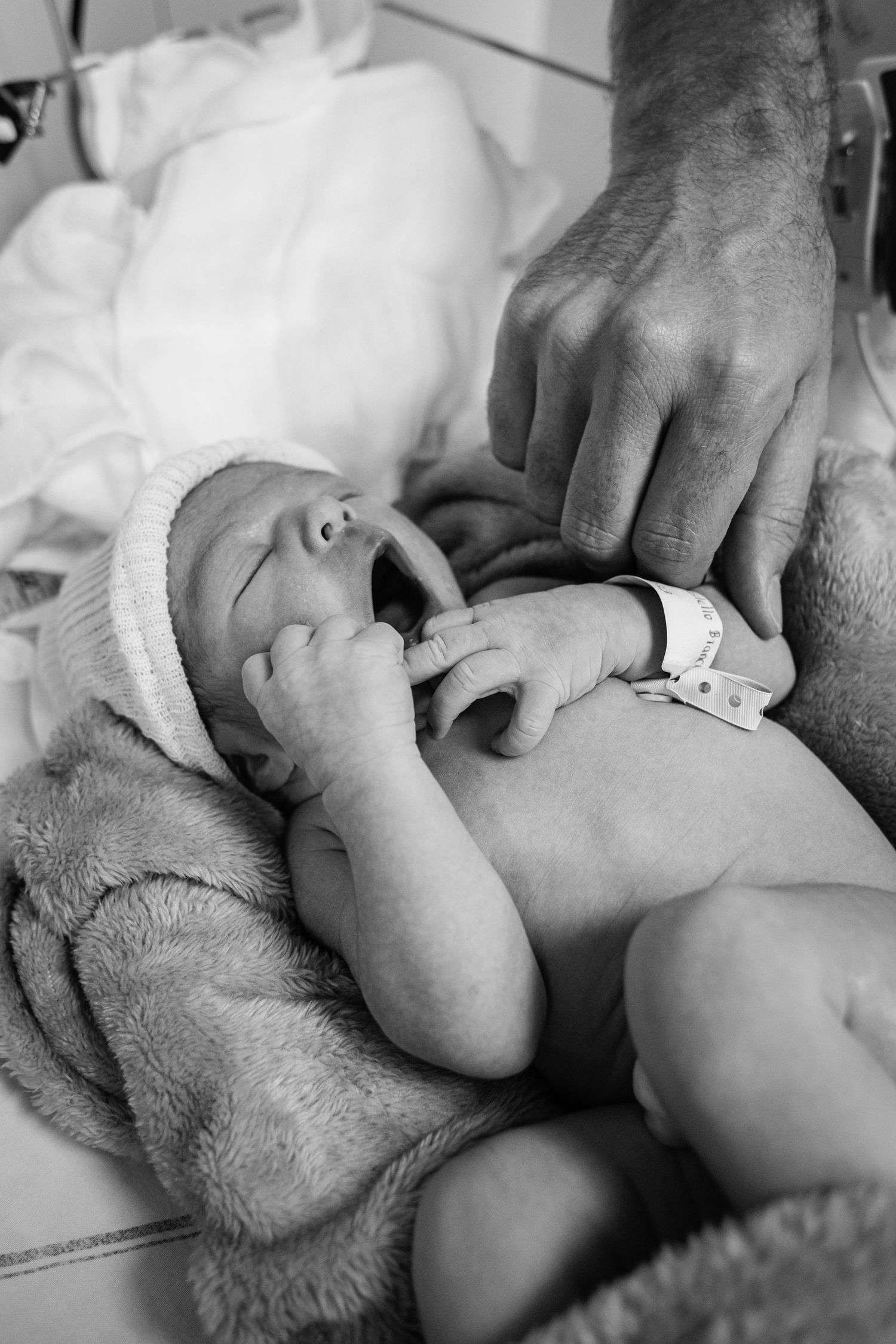 Black and white image of newborn in hospital wearing small hat and blanket.