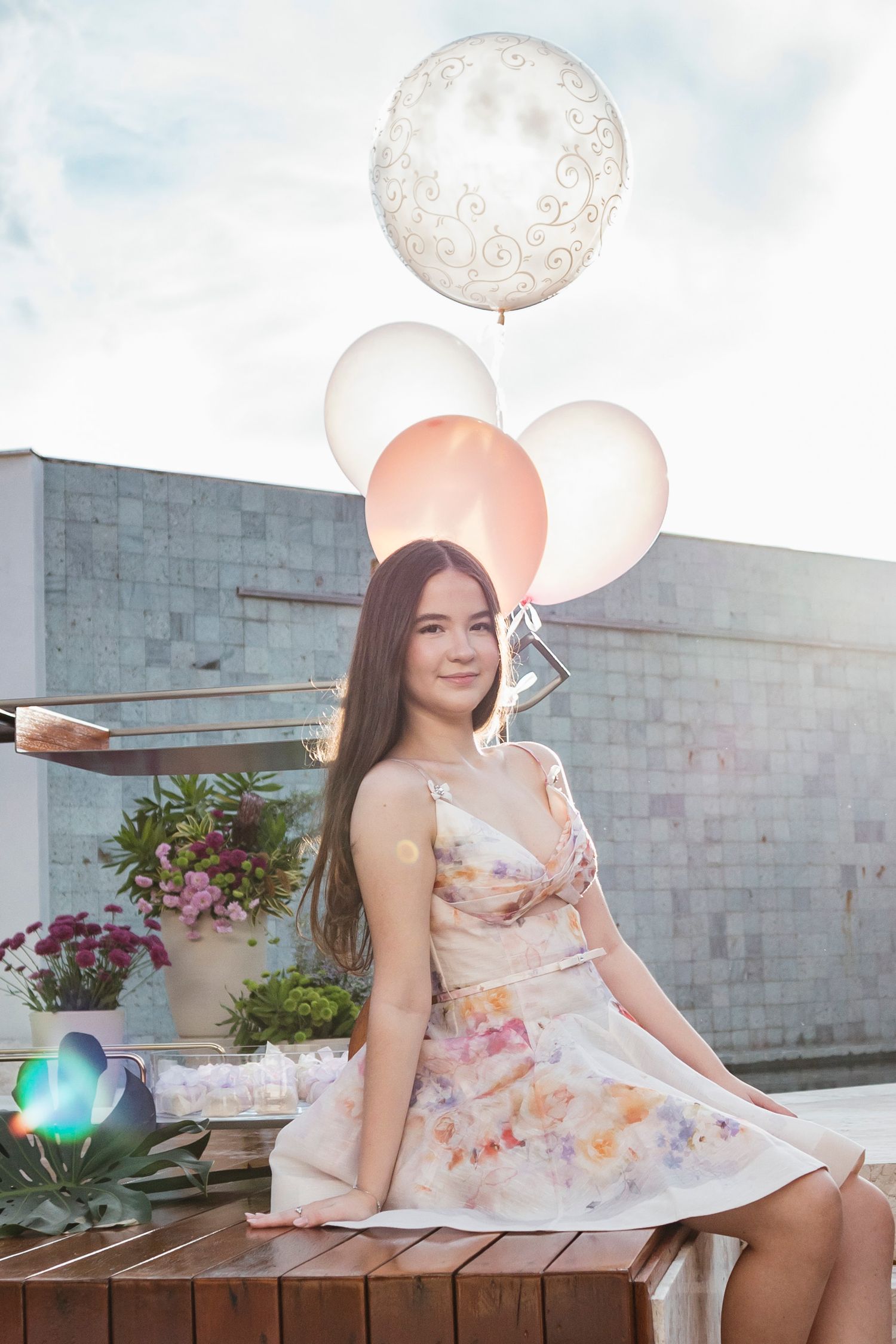 A floral dress photoshoot with pink and white balloons against a brick wall backdrop.