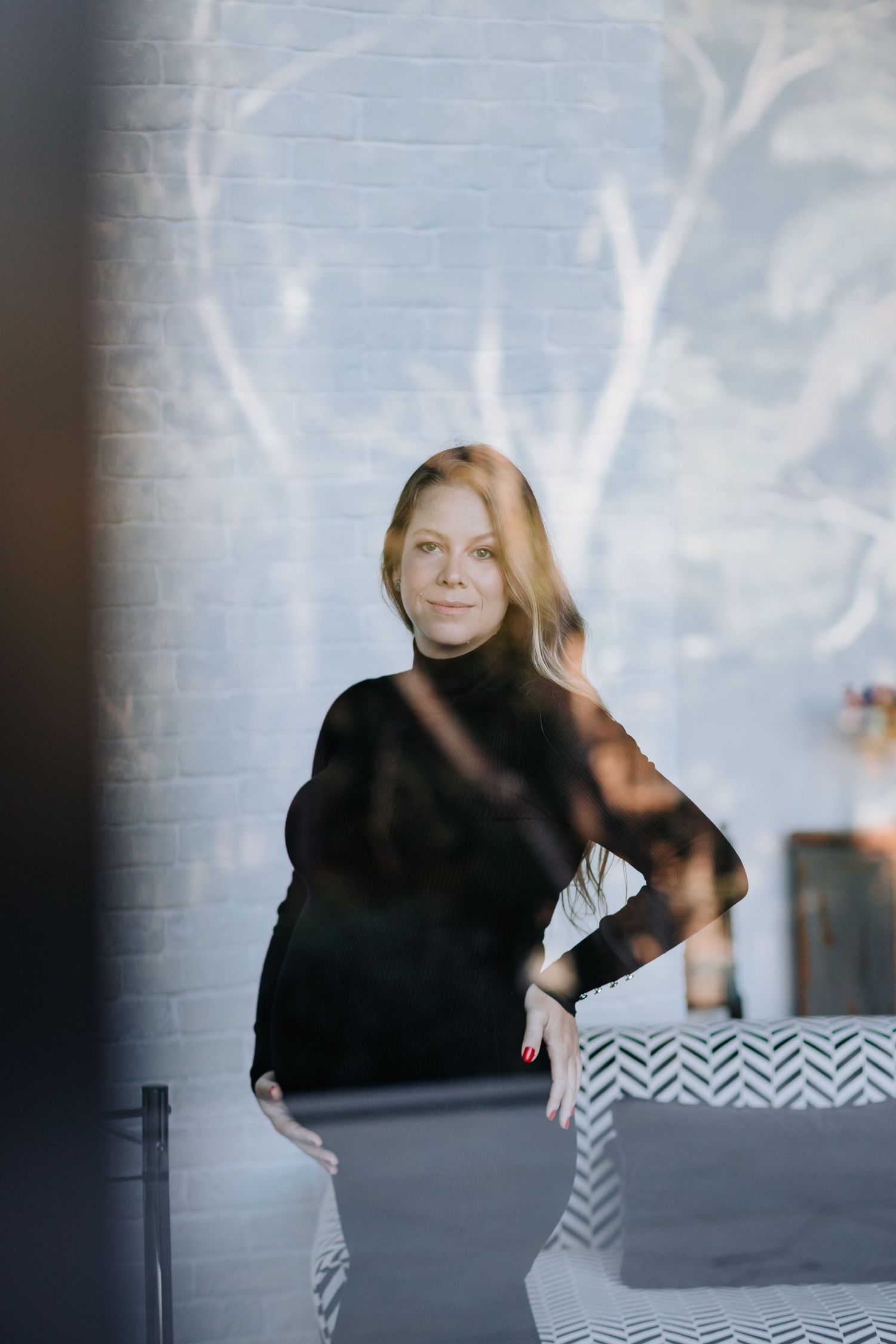 Artistic maternity photo with moody lighting showing expectant mother in black turtleneck against white wall.