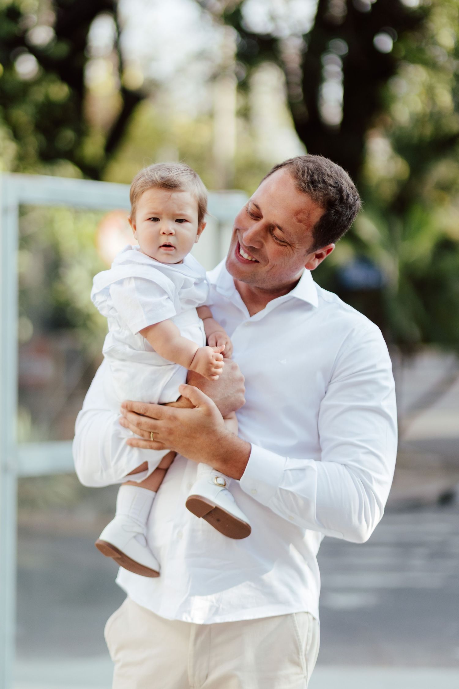 A parent in a white shirt holds and plays with a baby wearing white in a series of outdoor photos.