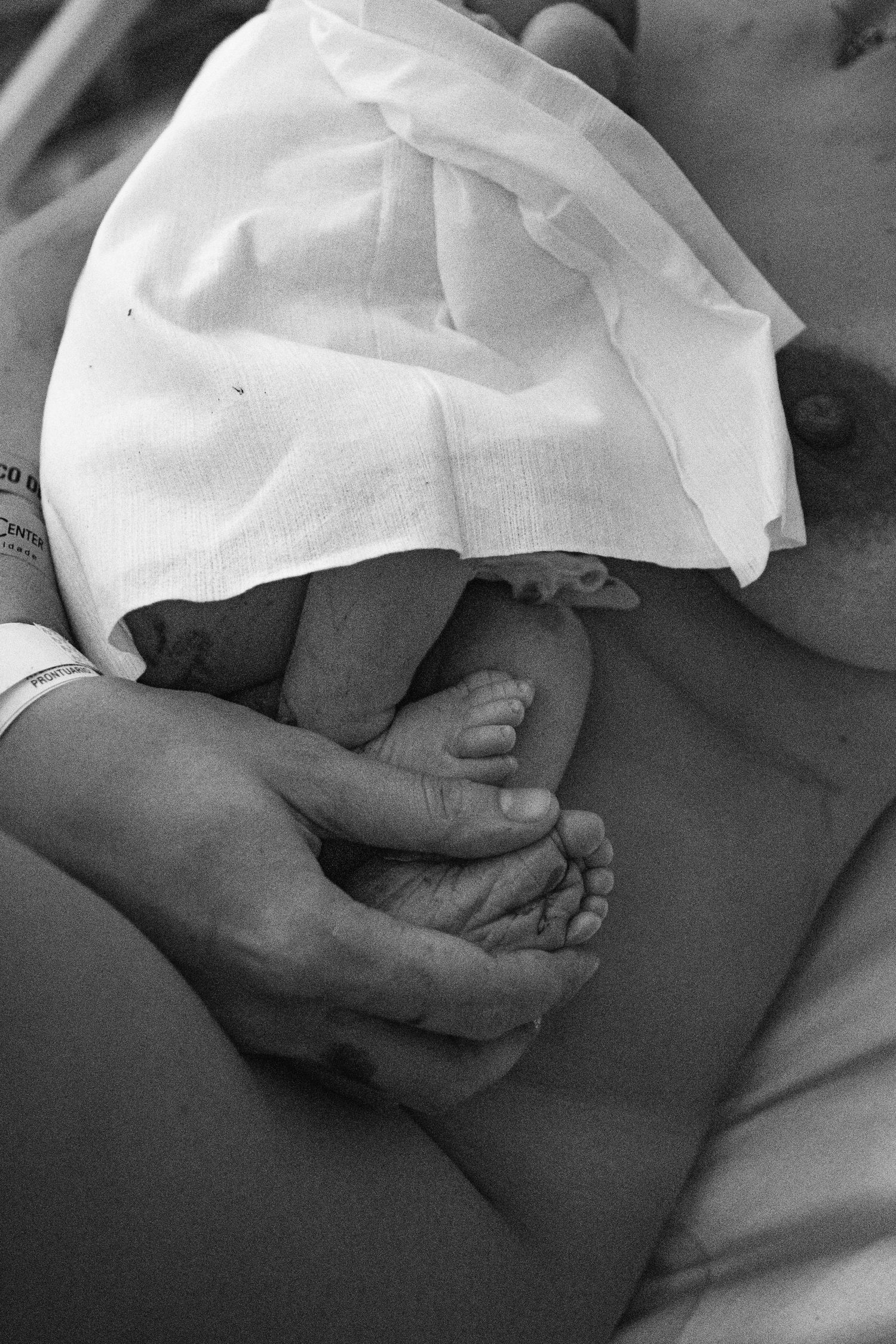 Black and white image of tiny newborn feet being gently held by caring hands.