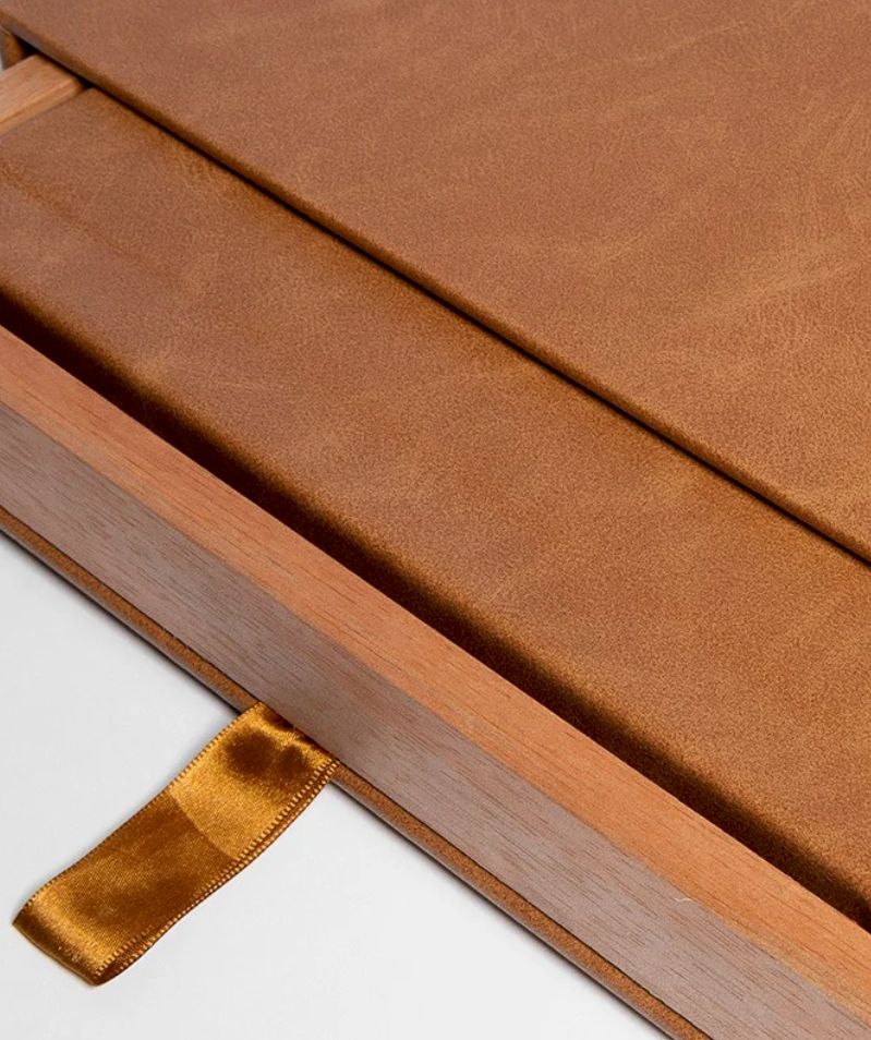 Close-up of a tan leather book in a wooden box with a gold satin ribbon bookmark tab.