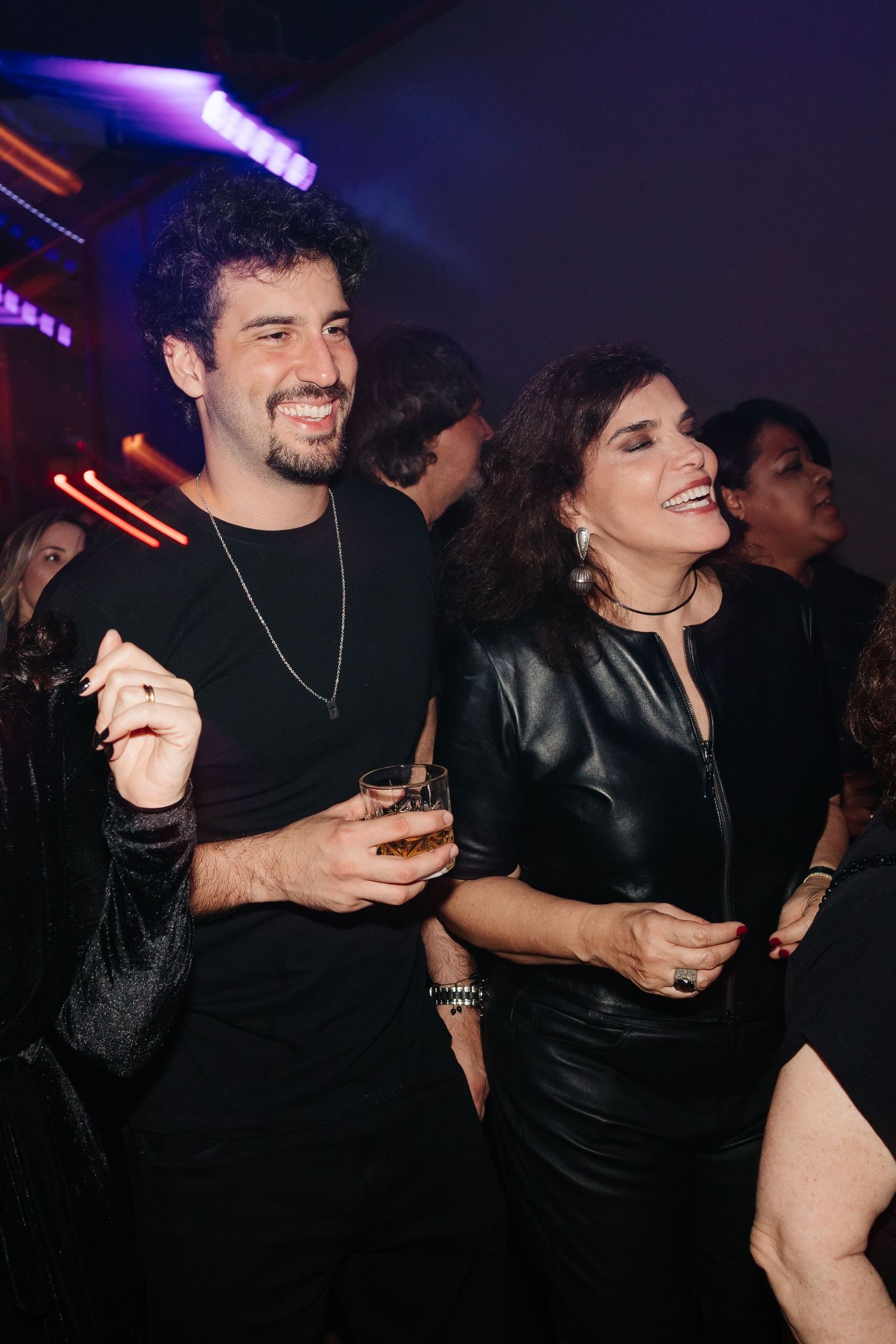 Two people enjoying a night out at a club, dressed in black outfits and smiling while holding drinks.