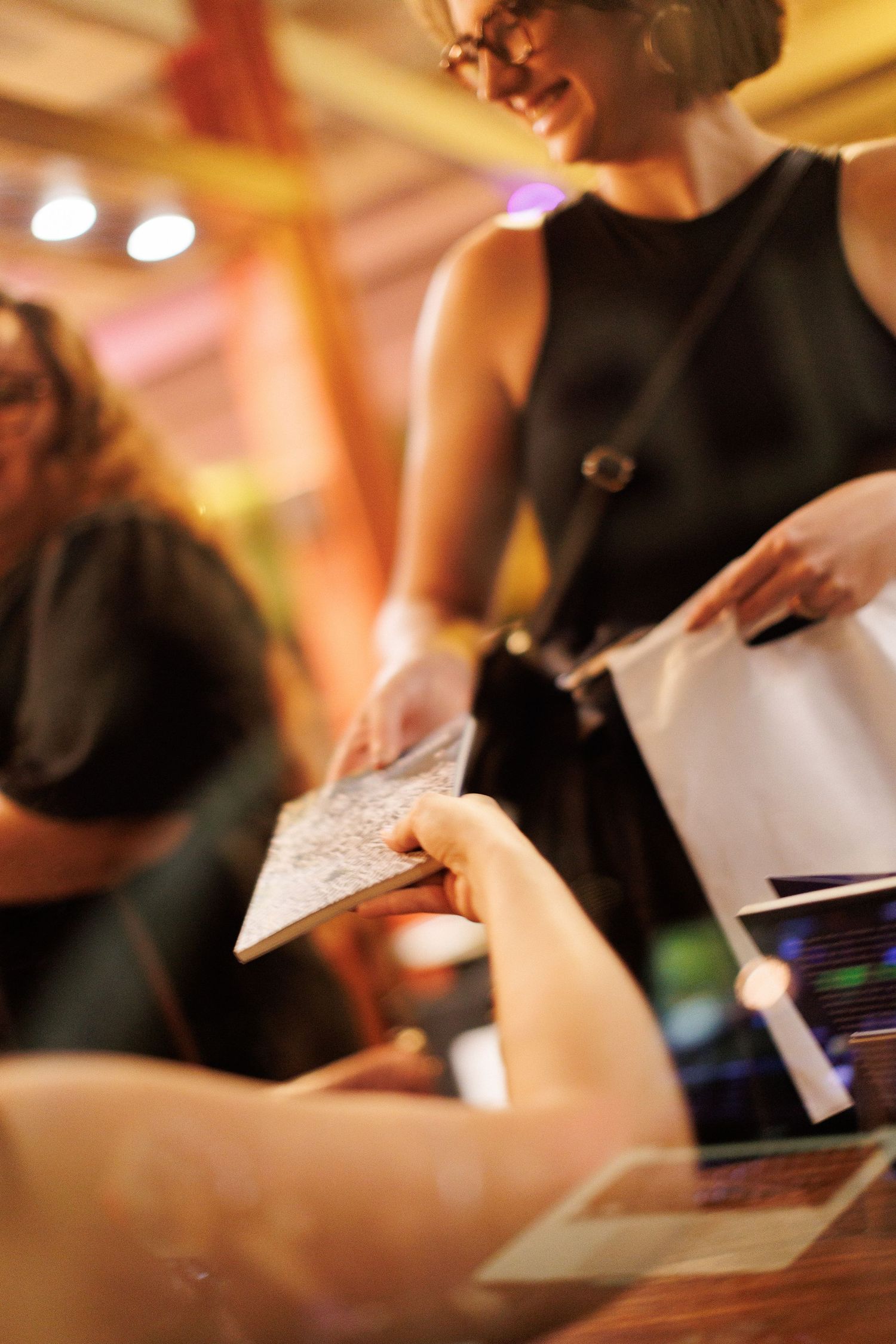 Woman in black dress smiling while exchanging documents at an event registration desk.