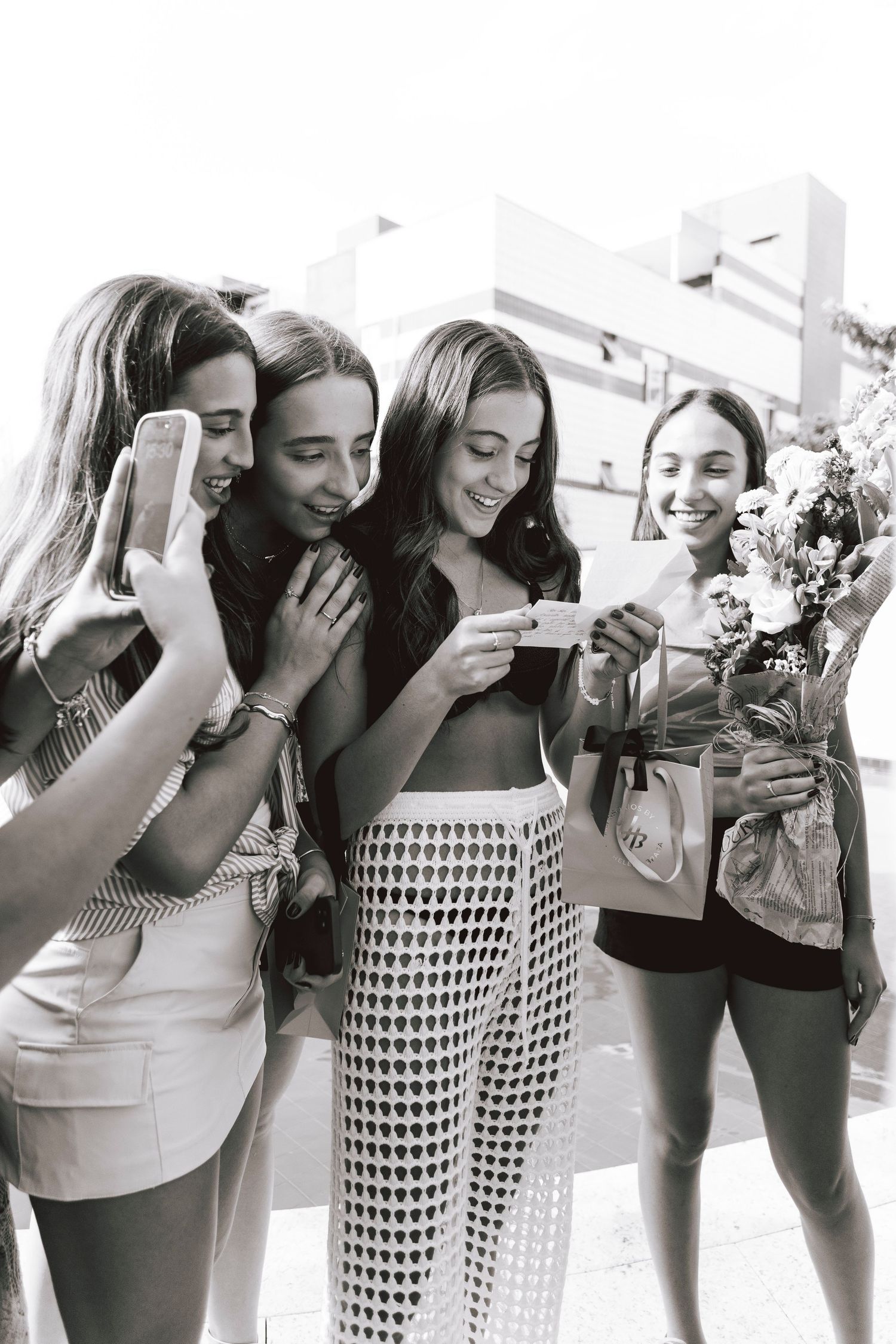 Group of friends excitedly gathered around looking at something on a sunny day.