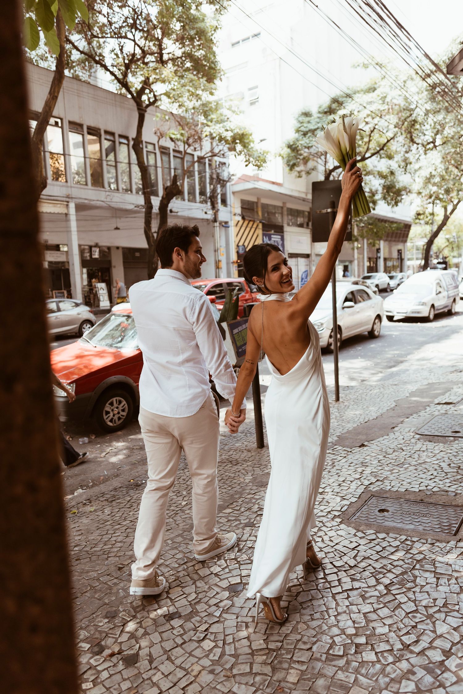 Person in white dress celebrates joyfully on cobblestone street.