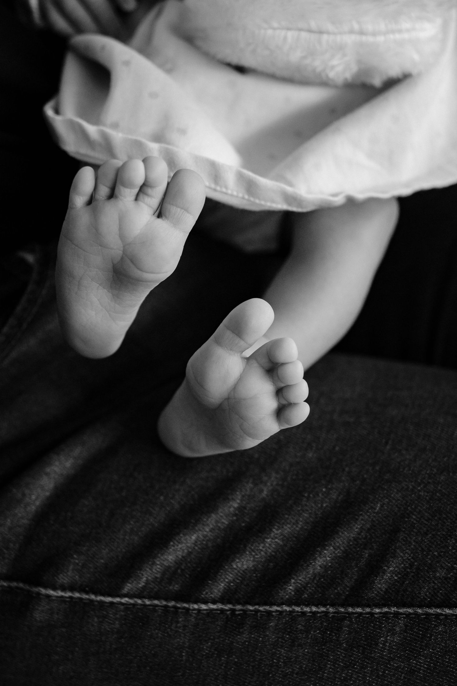 Black and white detail shot of tiny baby feet against dark fabric.