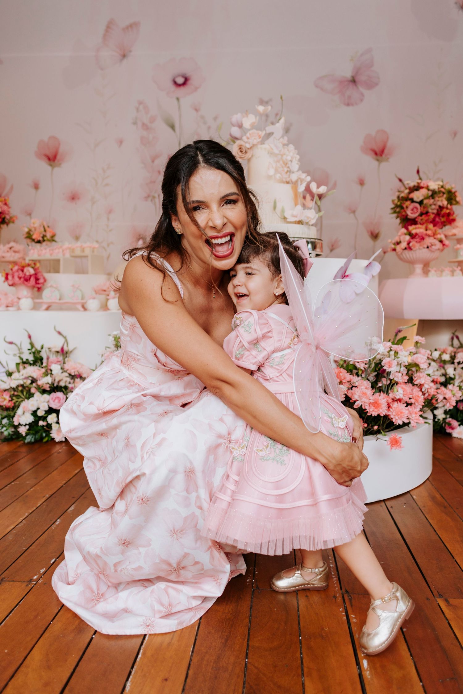 Sweet celebration moment with matching pink dresses against floral party backdrop.