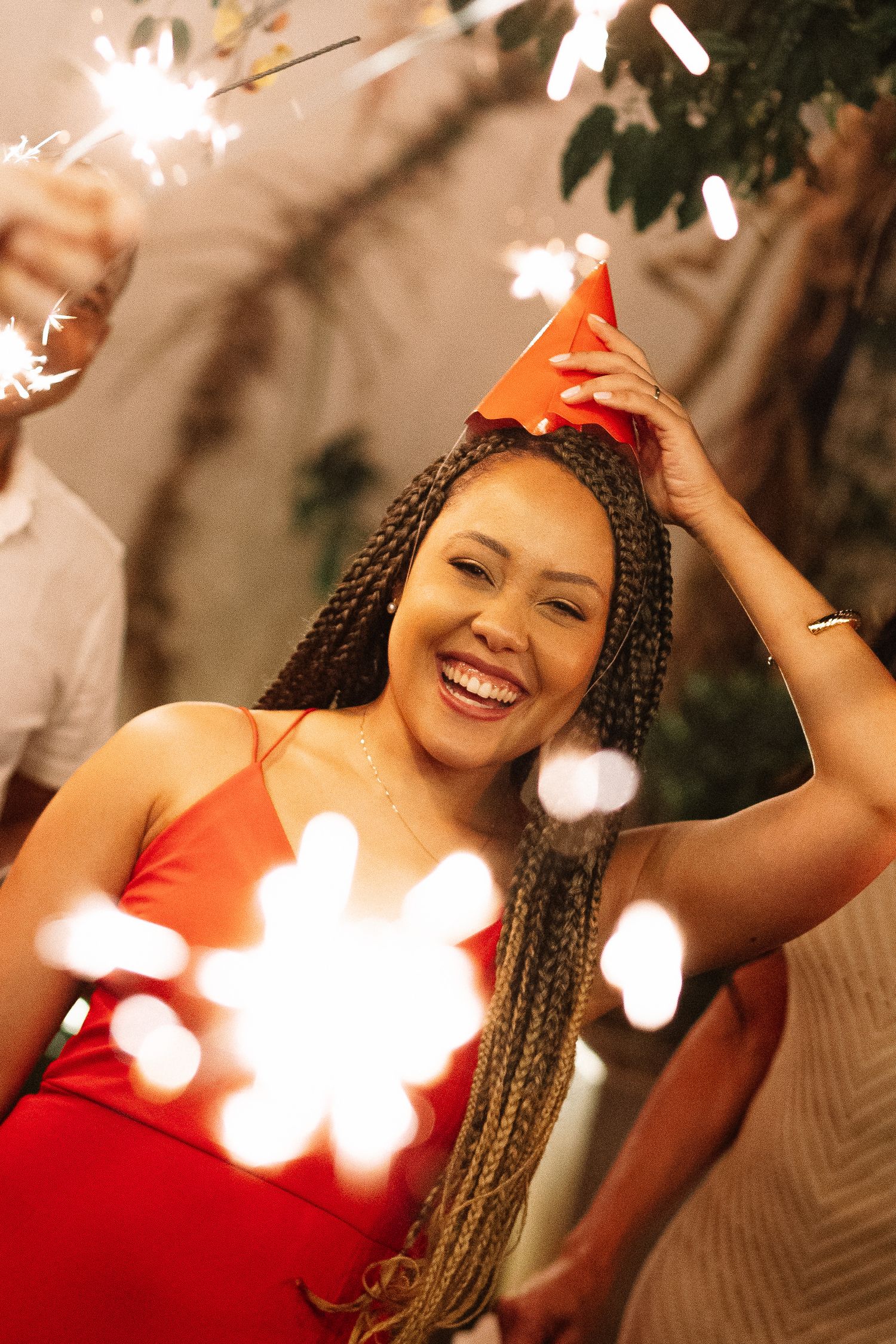 Woman in red dress and party hat smiling with sparklers at a celebration party.