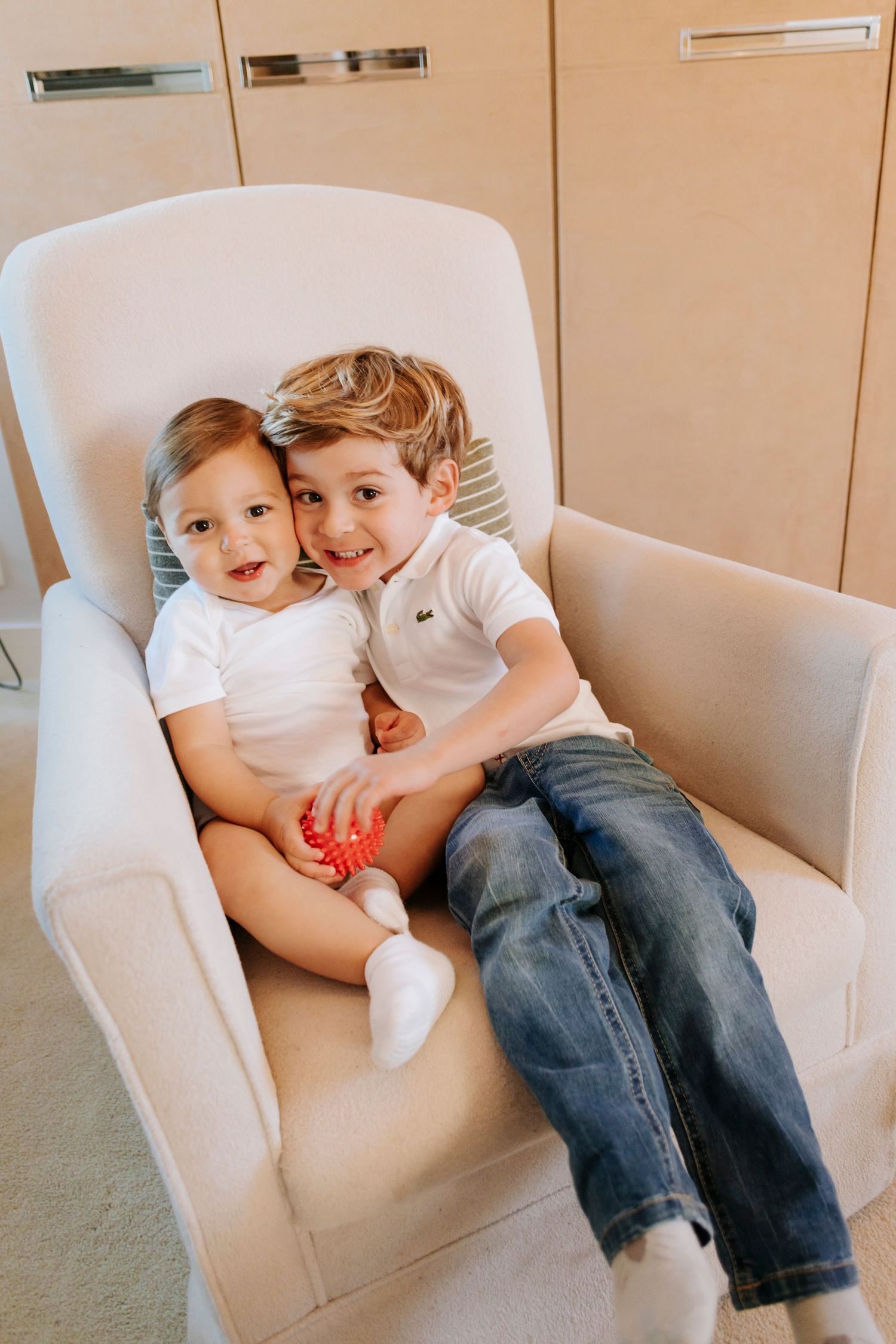Two children cuddling together on a white armchair in a series of candid photos.