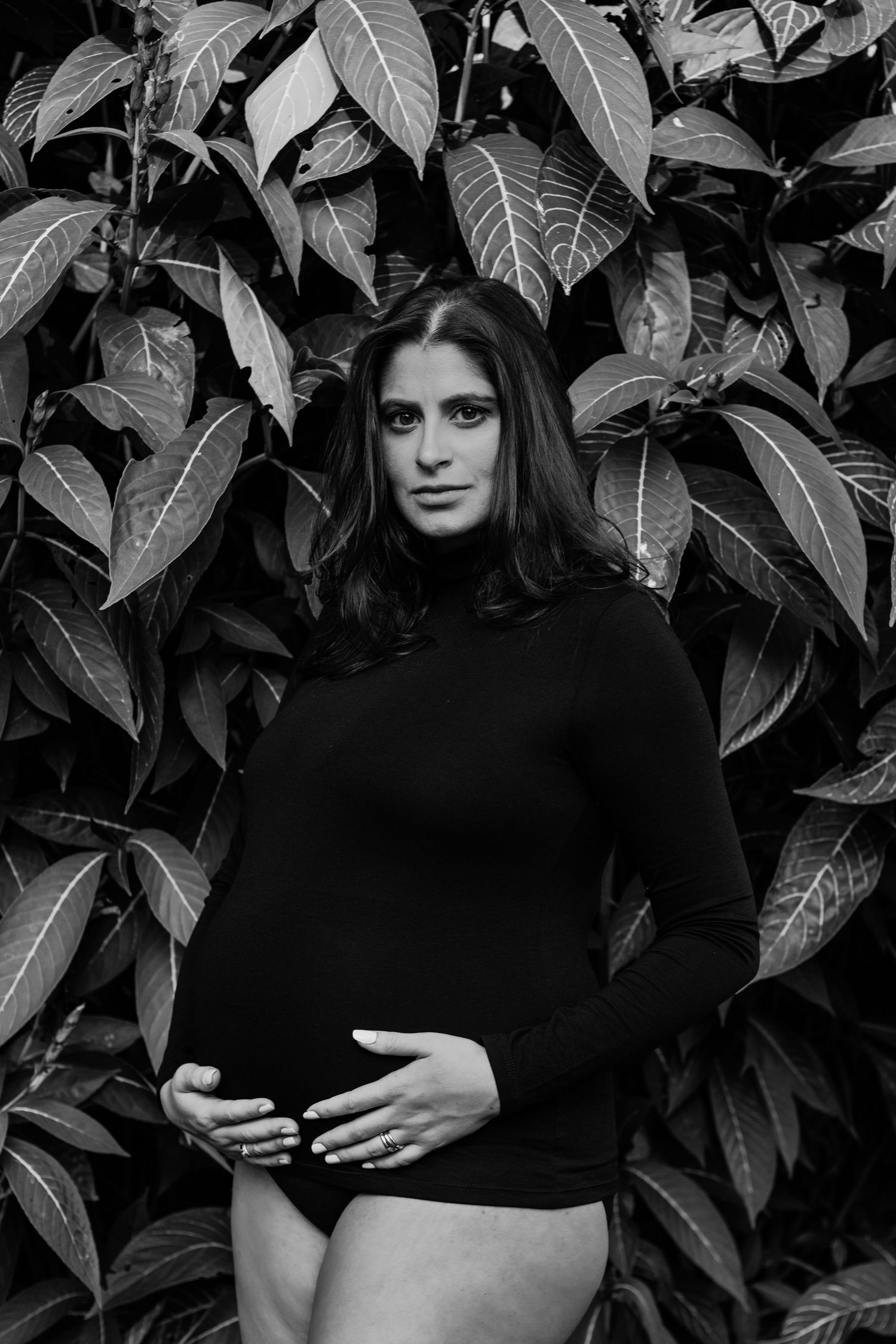 Four black and white photos show someone in dark clothing posing against a leafy background wall.