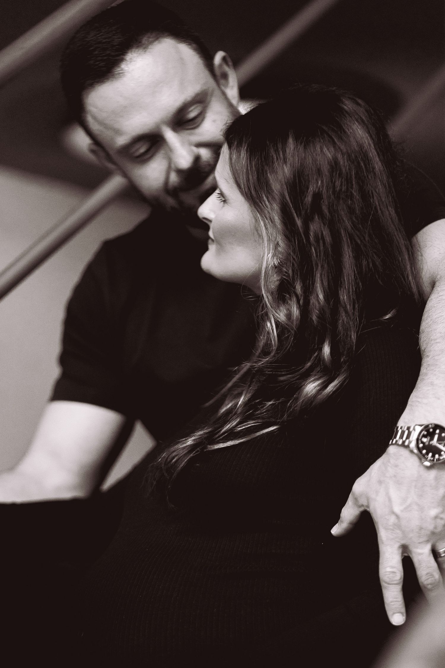 Intimate black and white photo of couple embracing, man holding woman from behind lovingly.