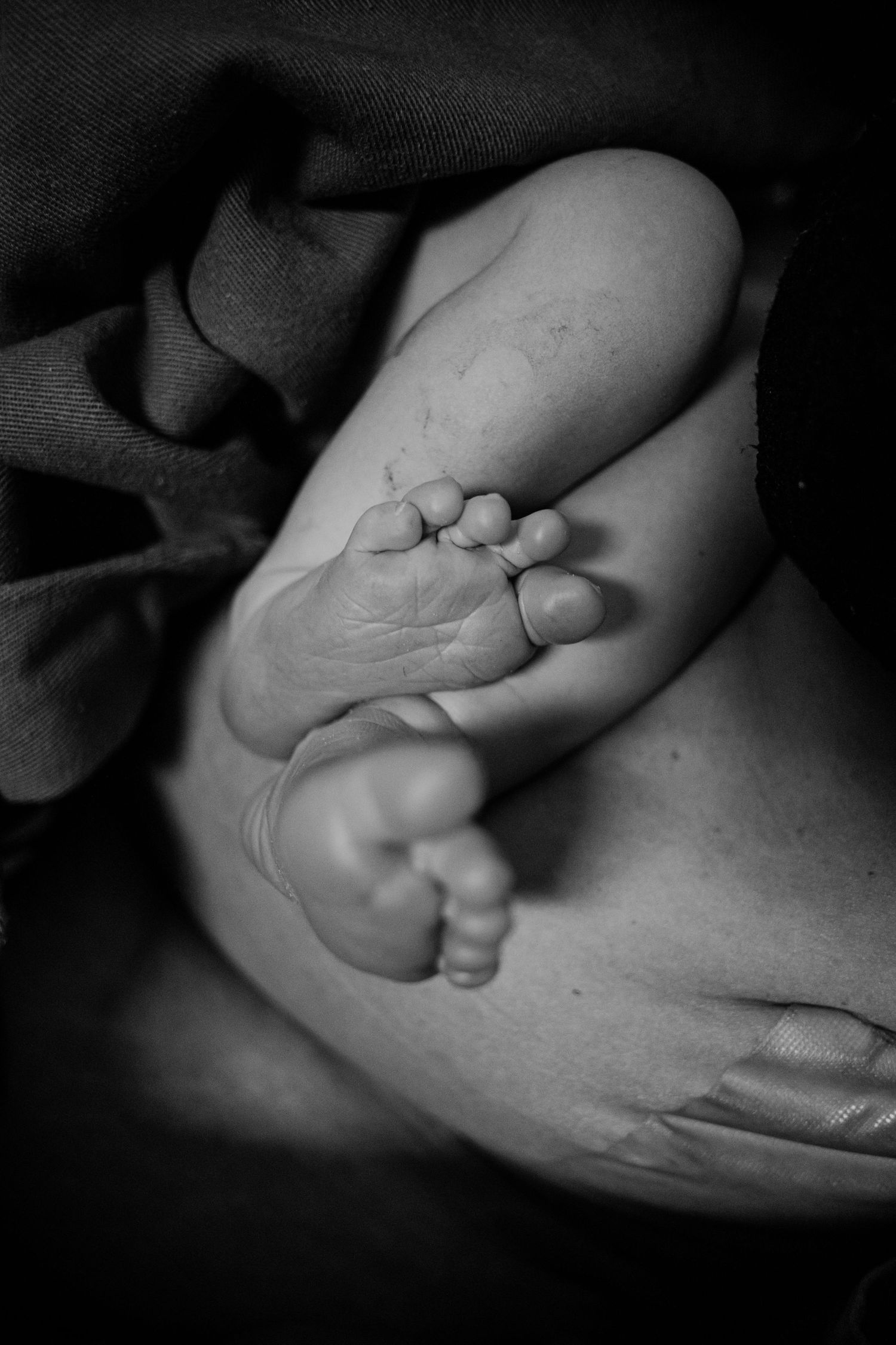 Black and white macro shot of baby feet nestled in gentle hands against dark fabric.
