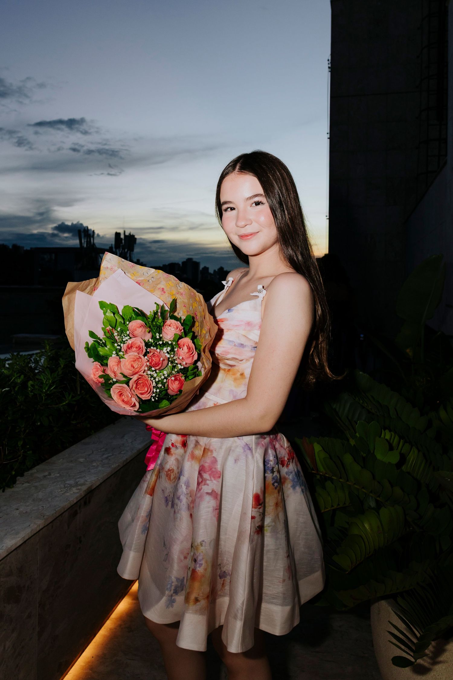 Evening portrait with a bouquet of pink roses against a sunset sky.