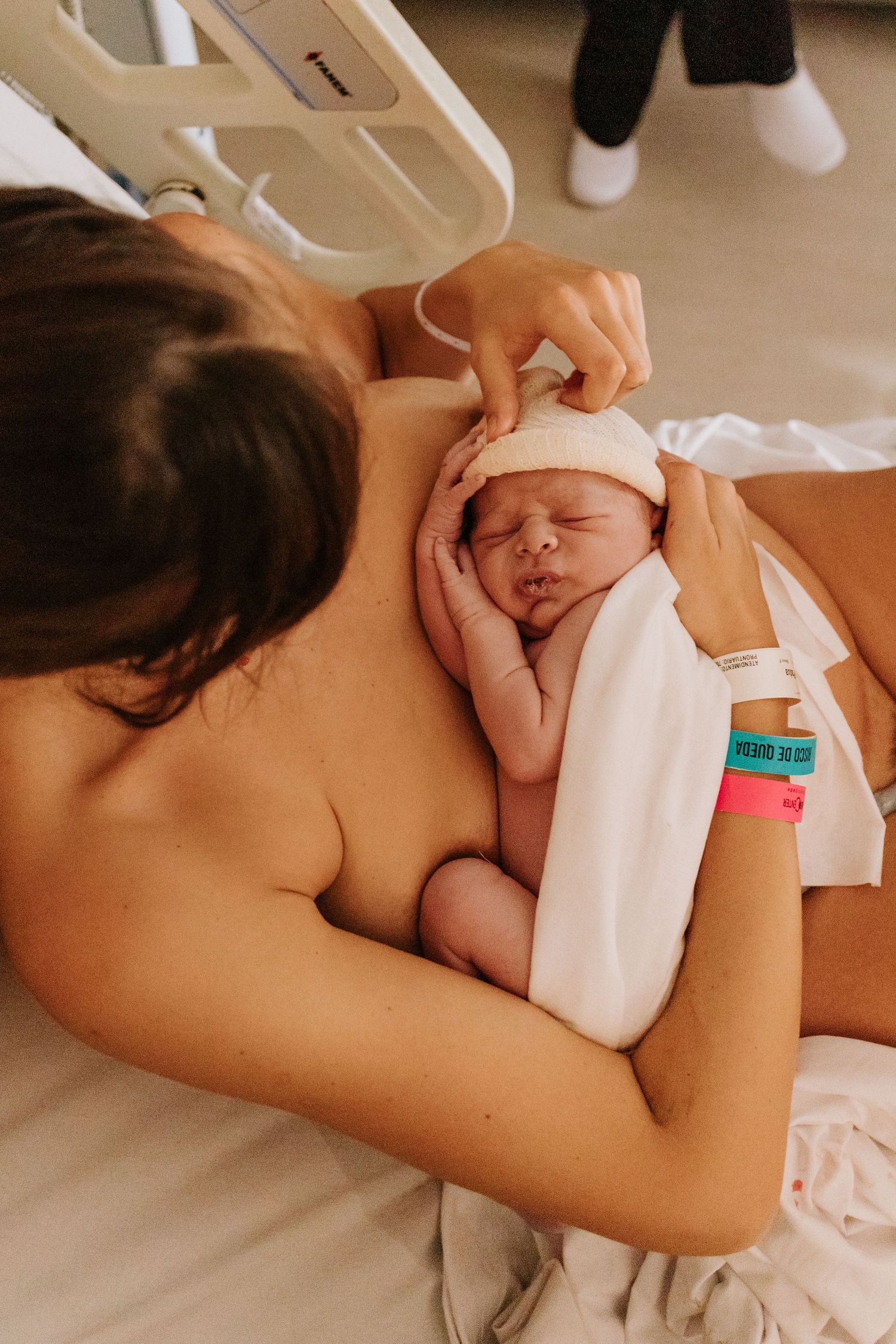 A newborn baby wrapped in white cloth being cradled close during skin-to-skin contact in a hospital setting.