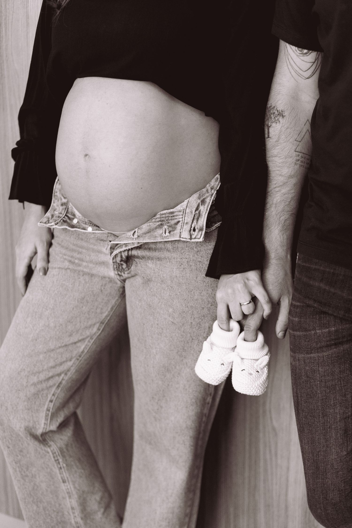 Black and white photo of pregnant woman and partner holding tiny baby shoes, maternity announcement concept.