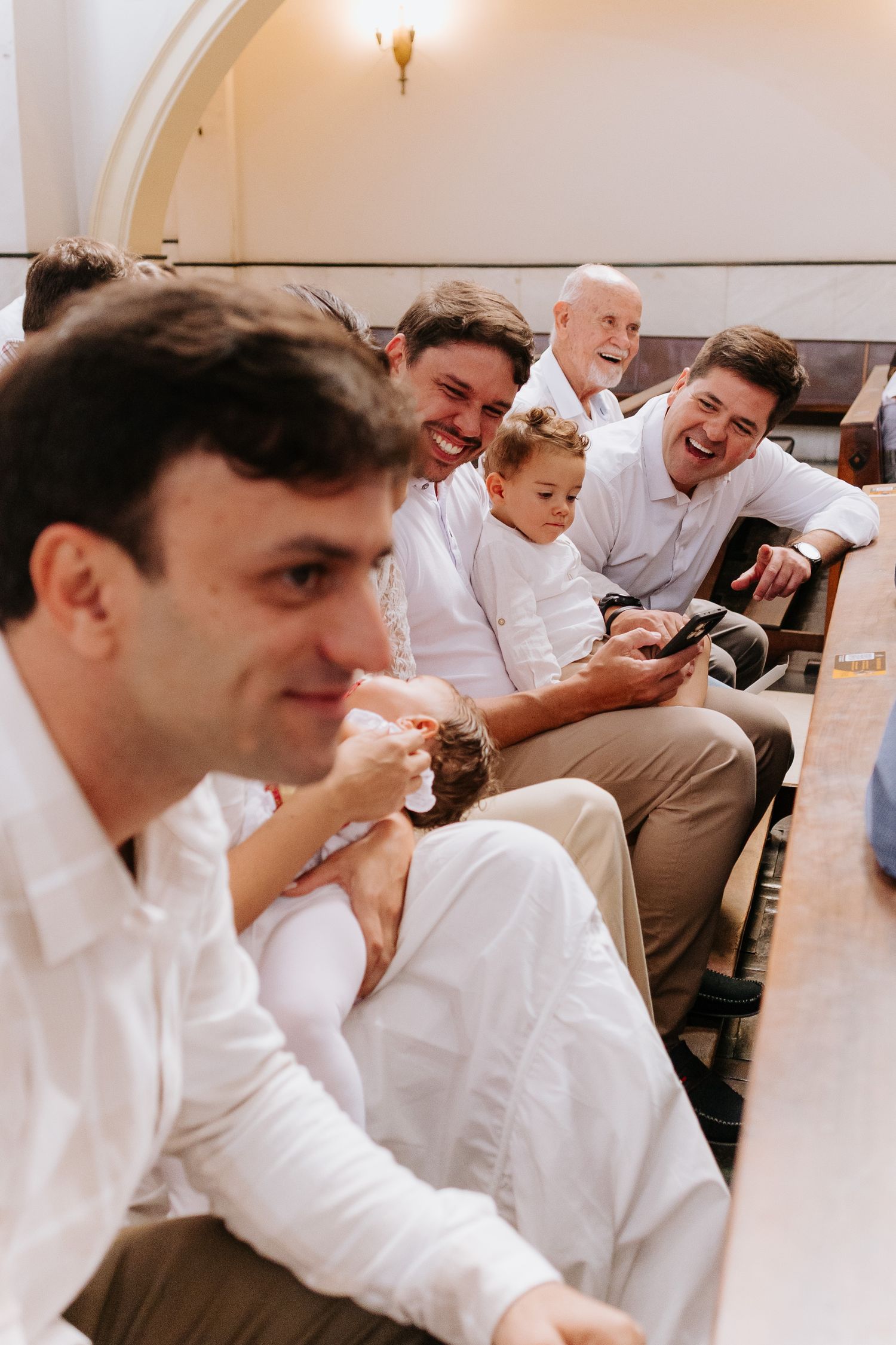 A group in white shirts sitting together and laughing while looking at something on a mobile device.