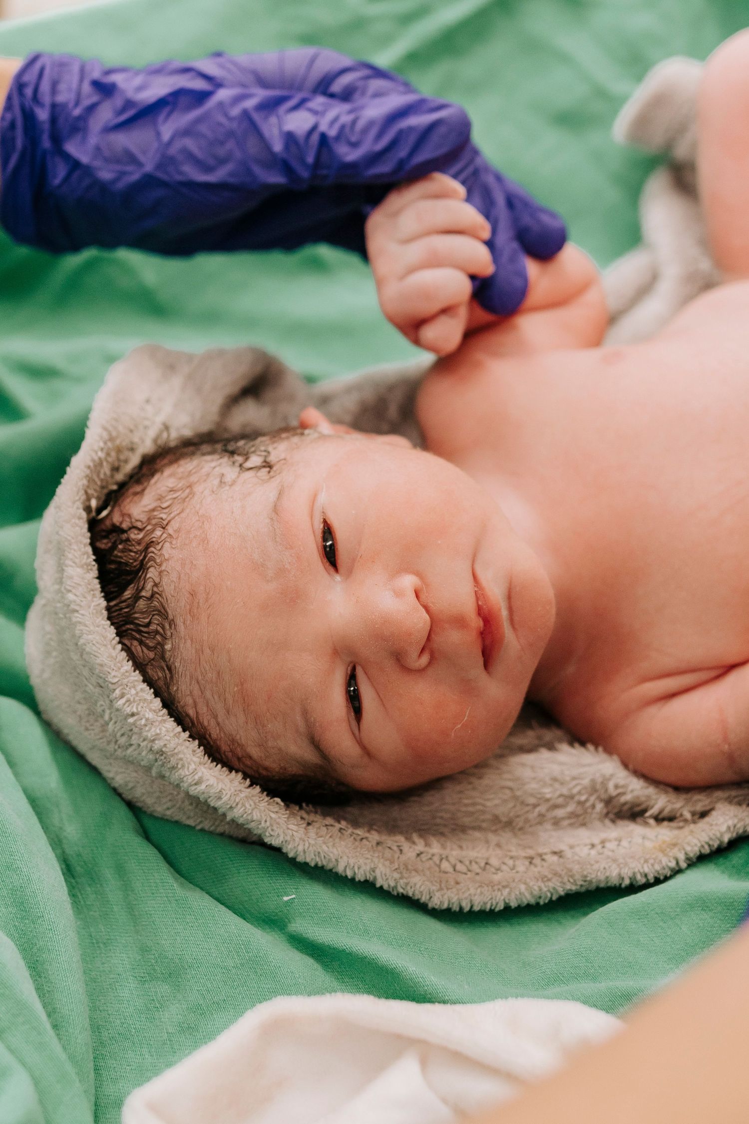 Fresh newborn baby lying on green medical sheet after delivery.