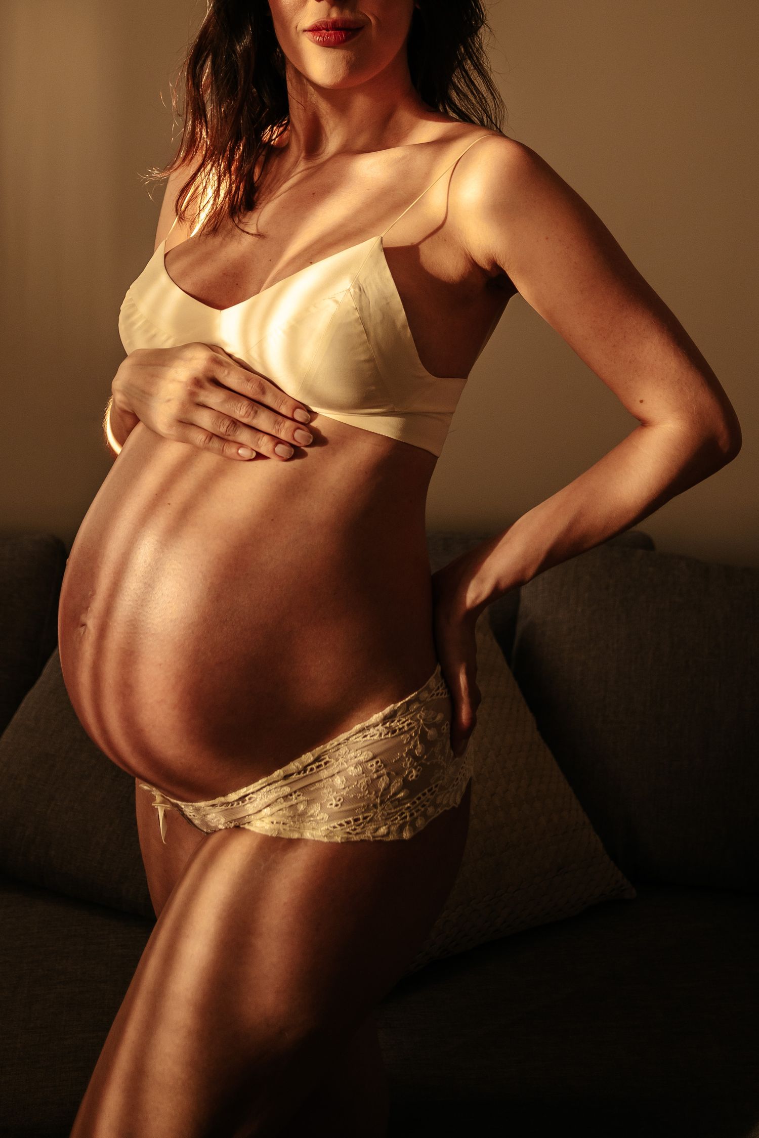 Close up of pregnant belly with hands tenderly placed in warm golden light.