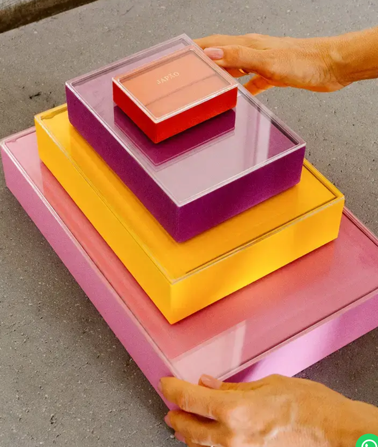 Colorful stacked acrylic boxes in pink, yellow, purple, and red, arranged by size with hands placing the lid.