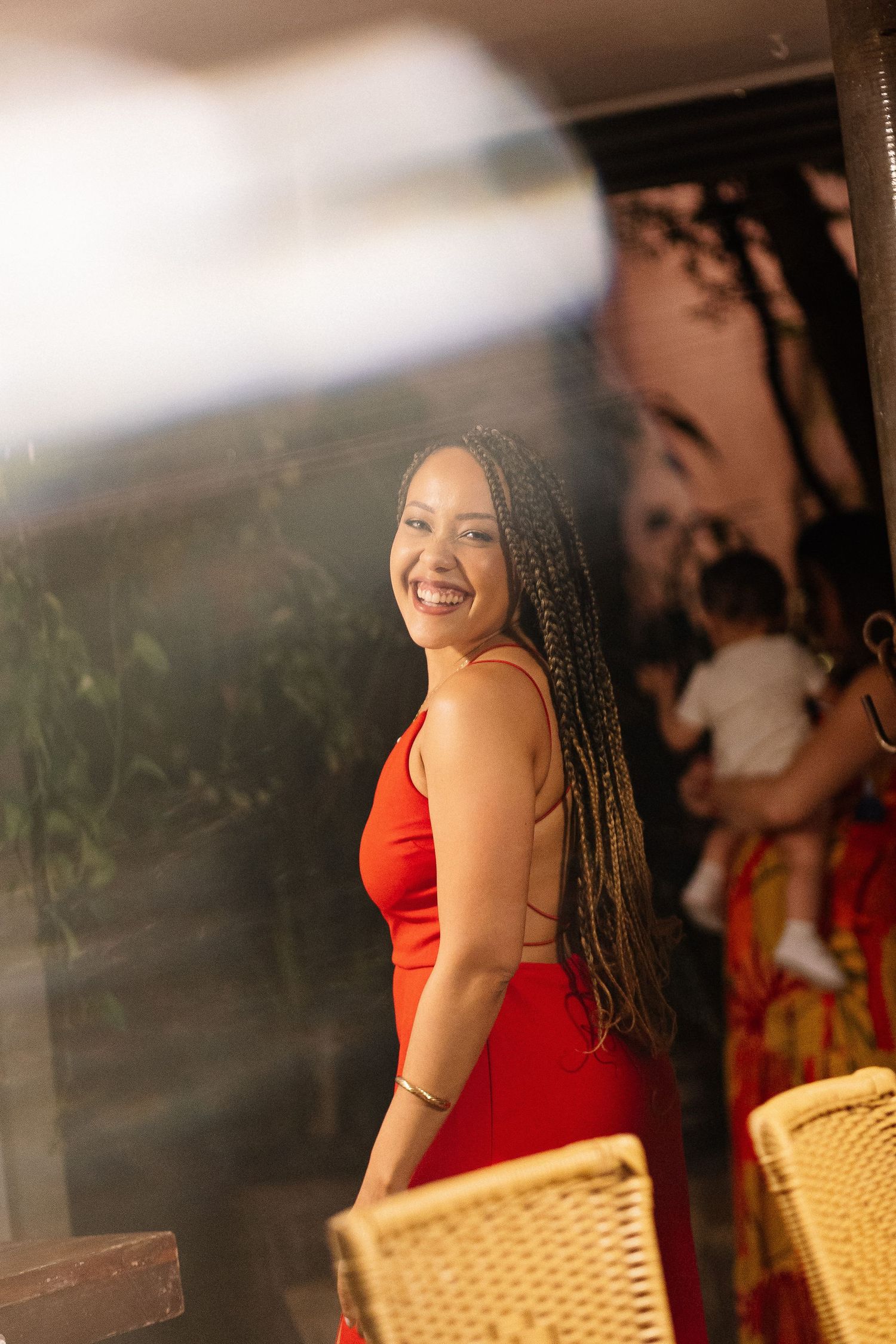 A person in a red dress sits at an outdoor cafe table with a joyful expression.