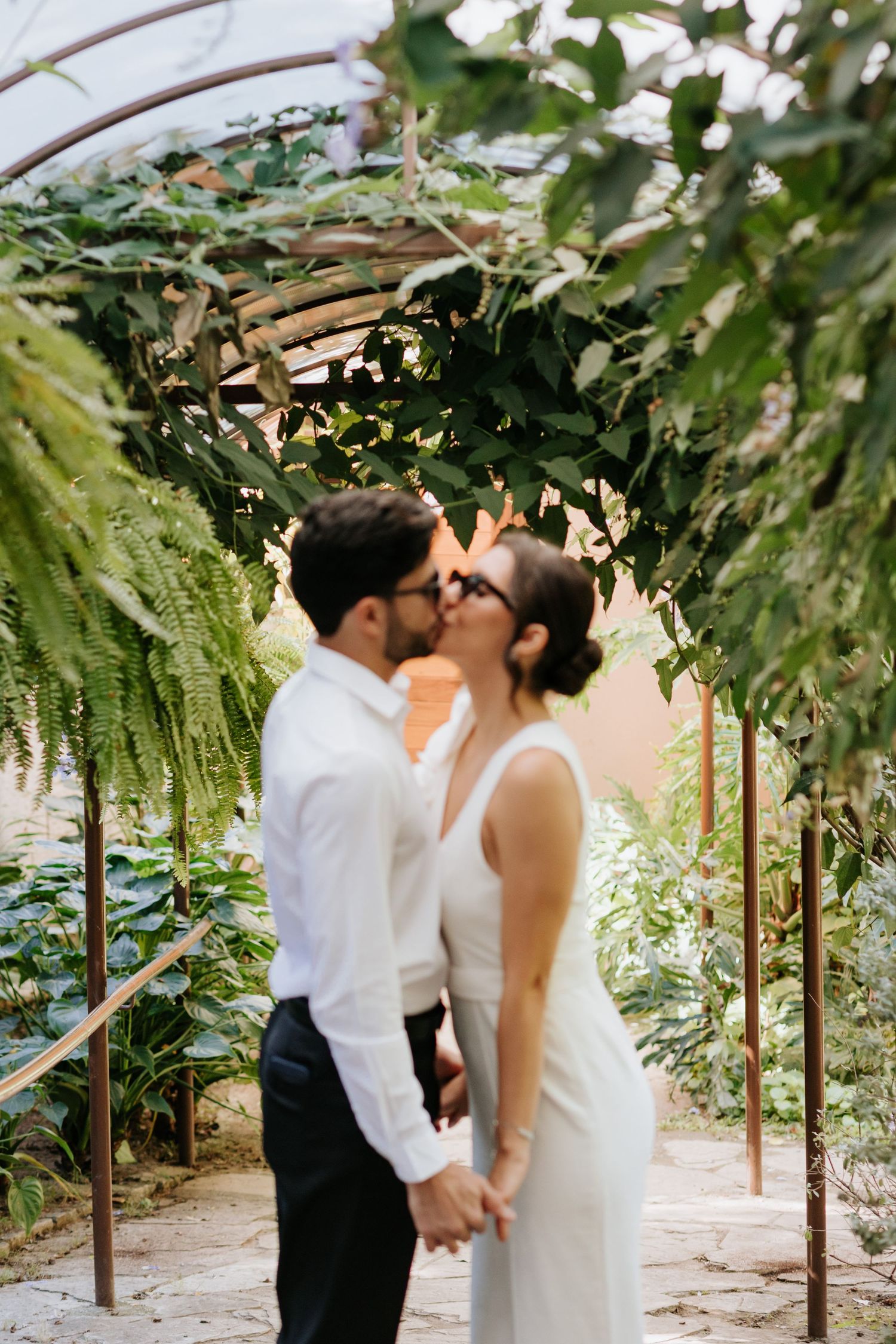 A couple sharing a tender moment under an archway covered in hanging plants and greenery.