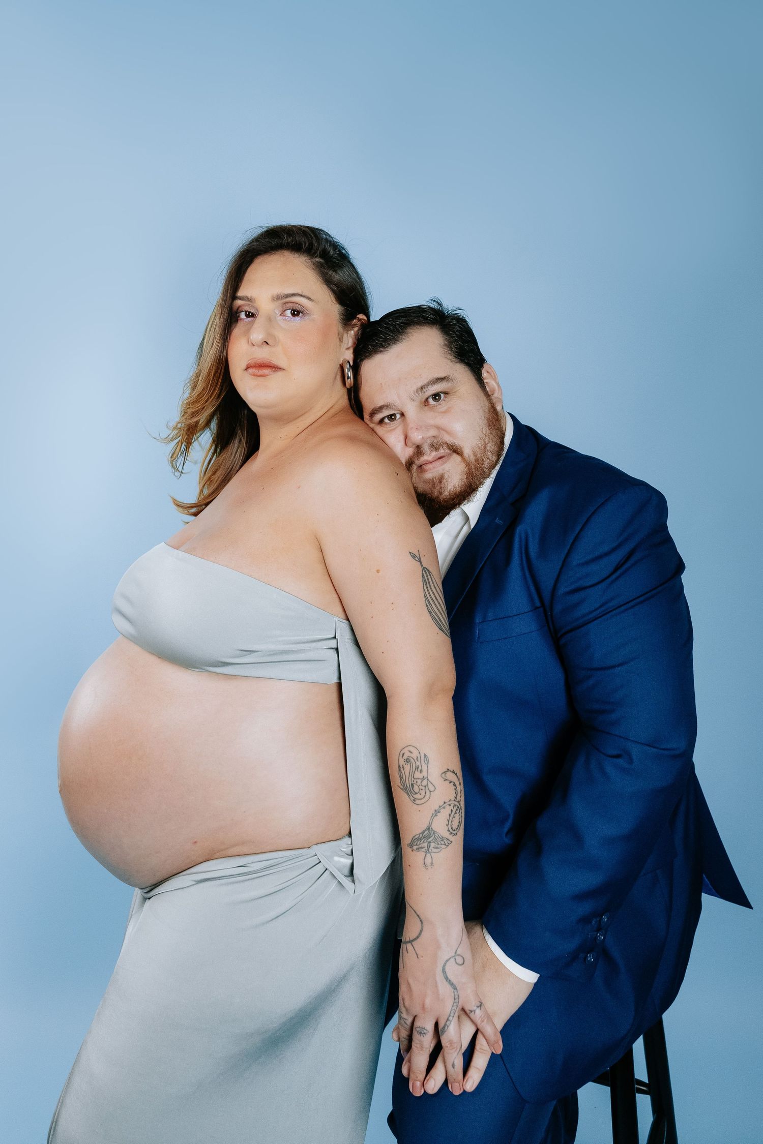 An intimate maternity portrait of a couple against a light blue studio background.