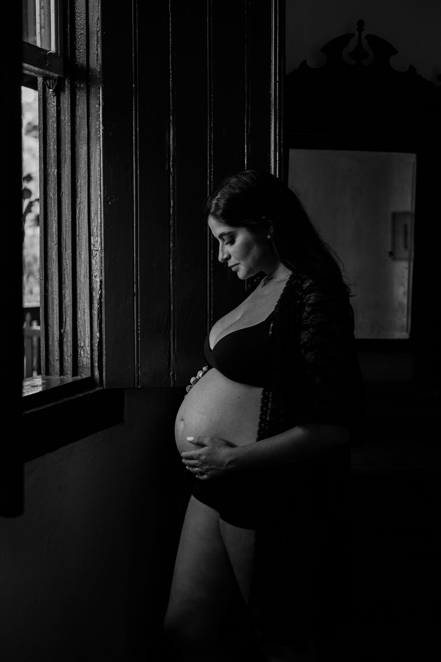 A moody black and white photo series showing a pregnant woman's silhouette against a window in intimate poses.