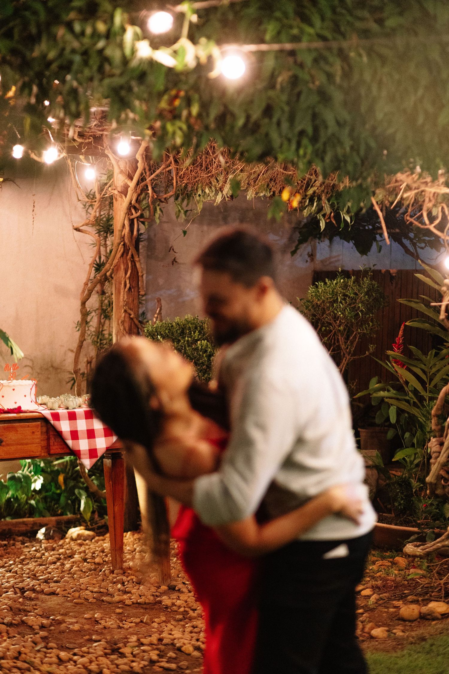 Couple dancing romantically in a garden at night under string lights with lush greenery and a festive table in the background.