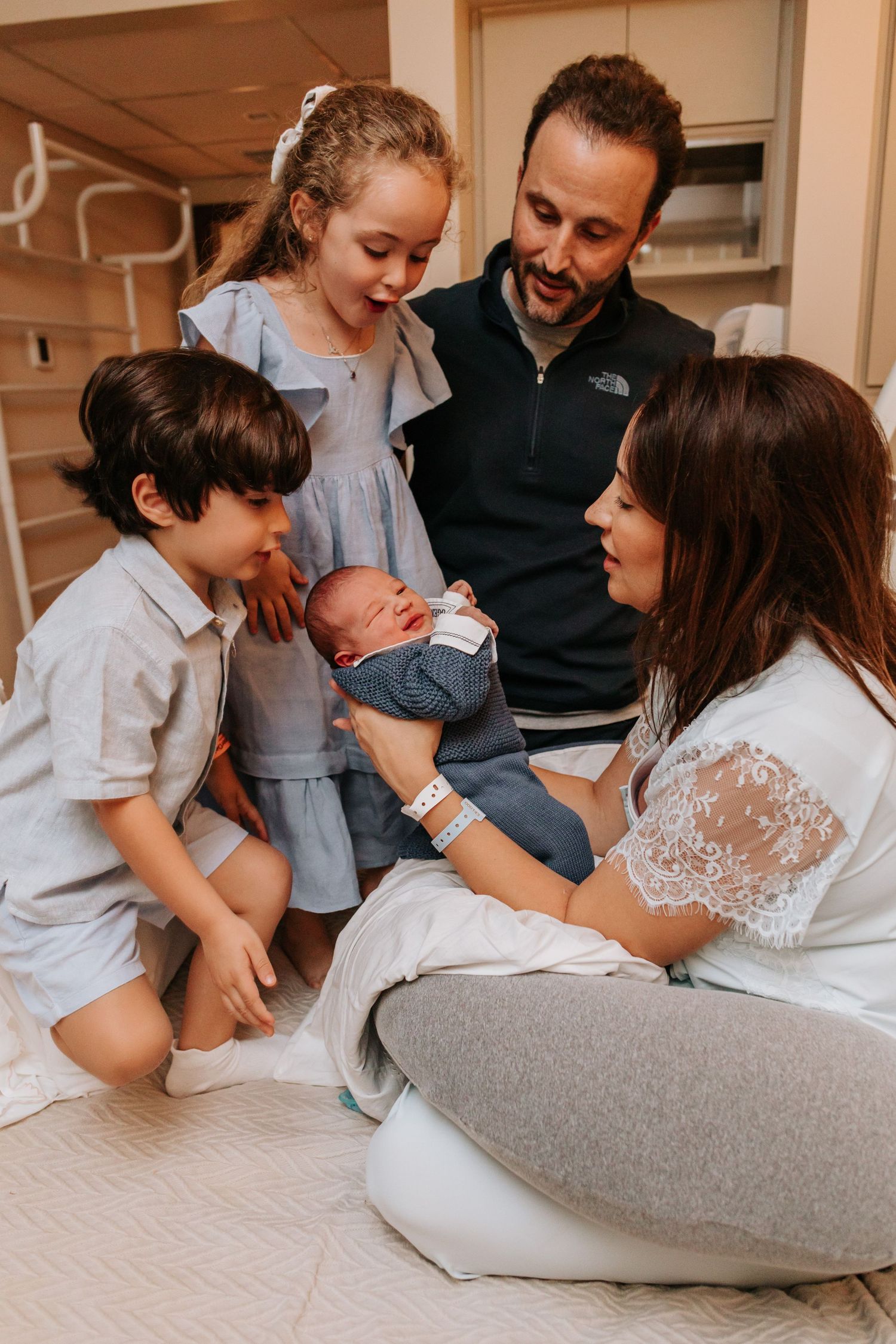 A family shares tender moments together while relaxing on a cozy bed in matching white outfits.