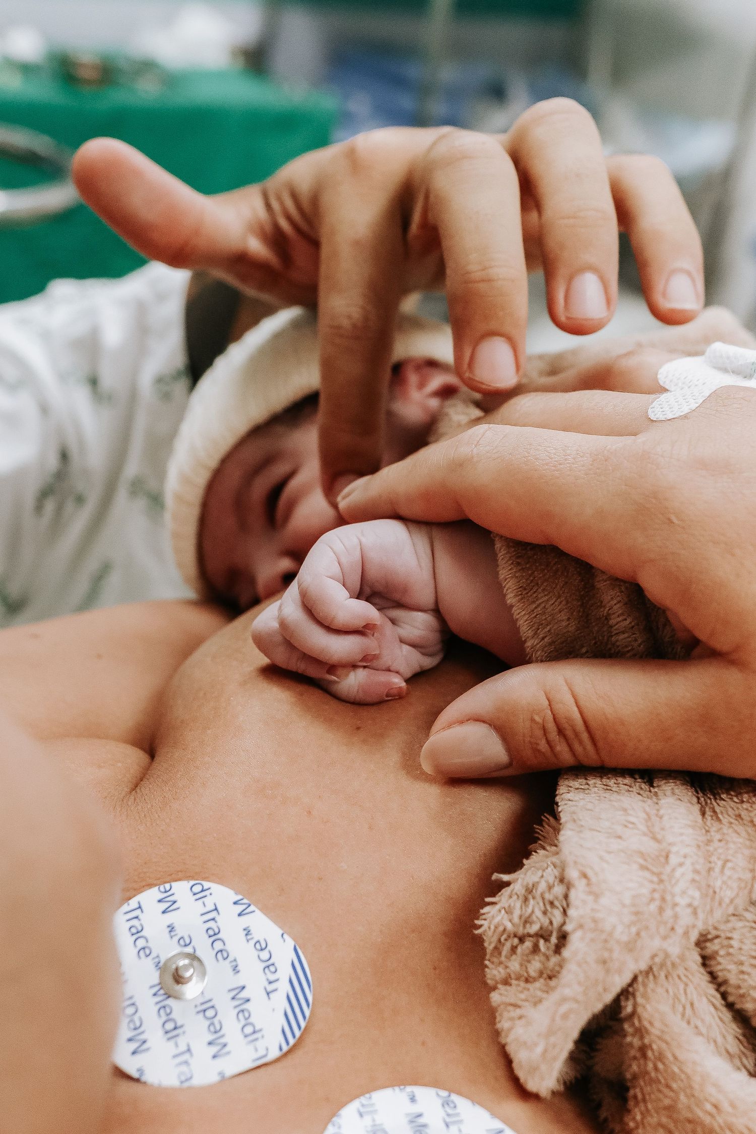 Close-up of newborn baby's tiny hand grasping adult finger during skin-to-skin contact.