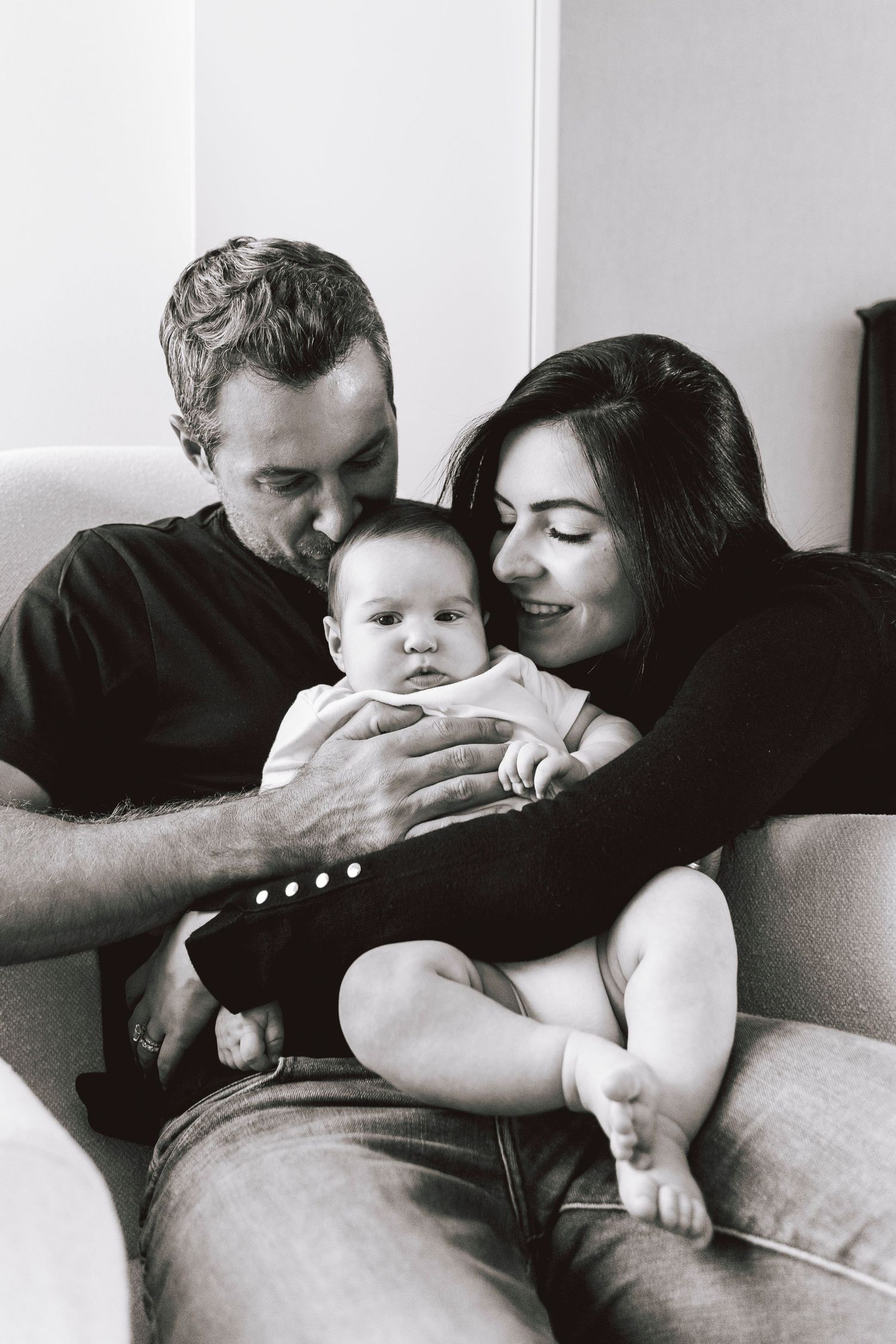 Black and white portrait of family snuggling with infant on couch.
